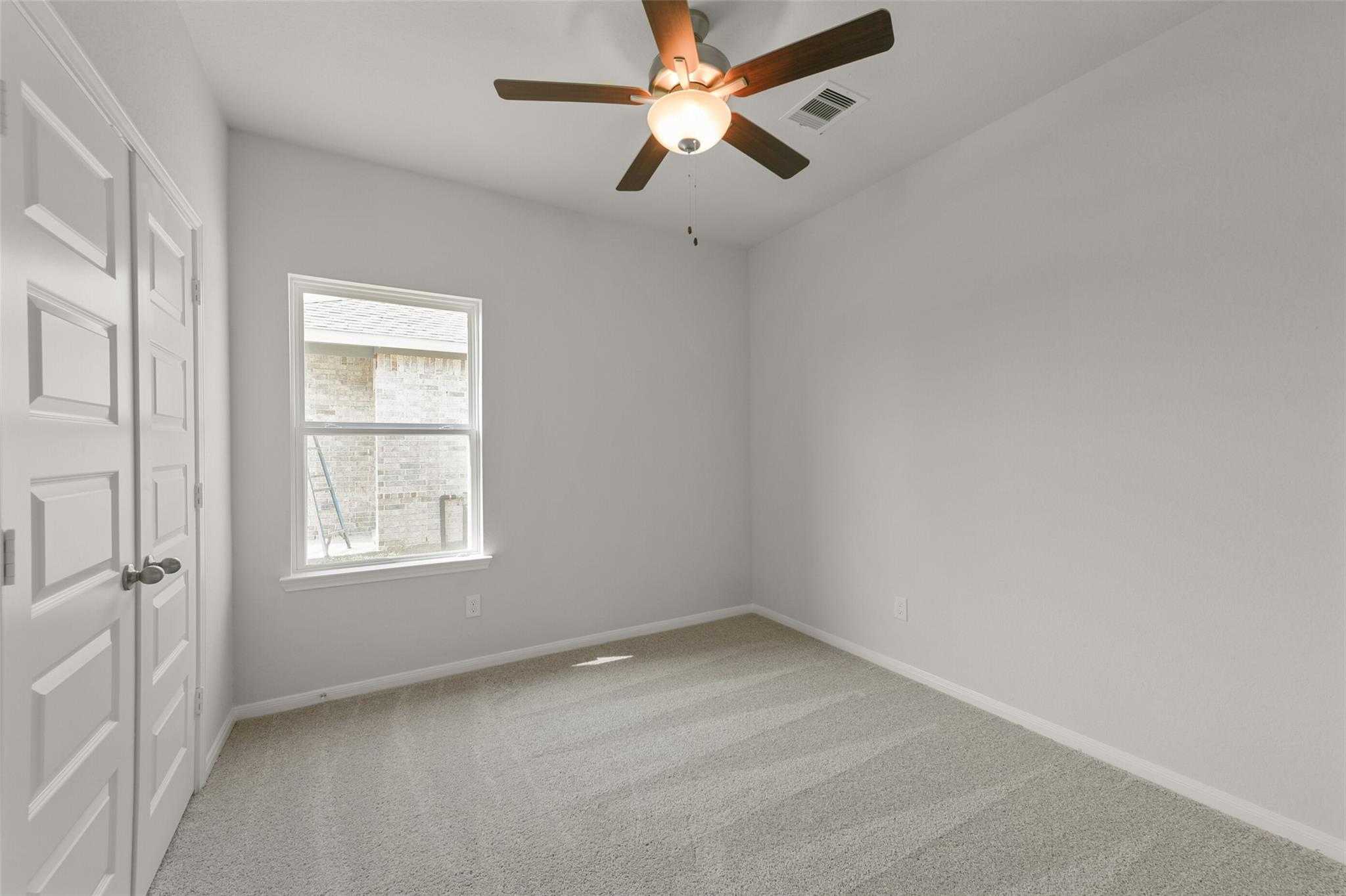 Bright secondary bedroom with ceiling fan, large window, double closet doors in Davidson Homes The Laguna B, Dayton, Texas