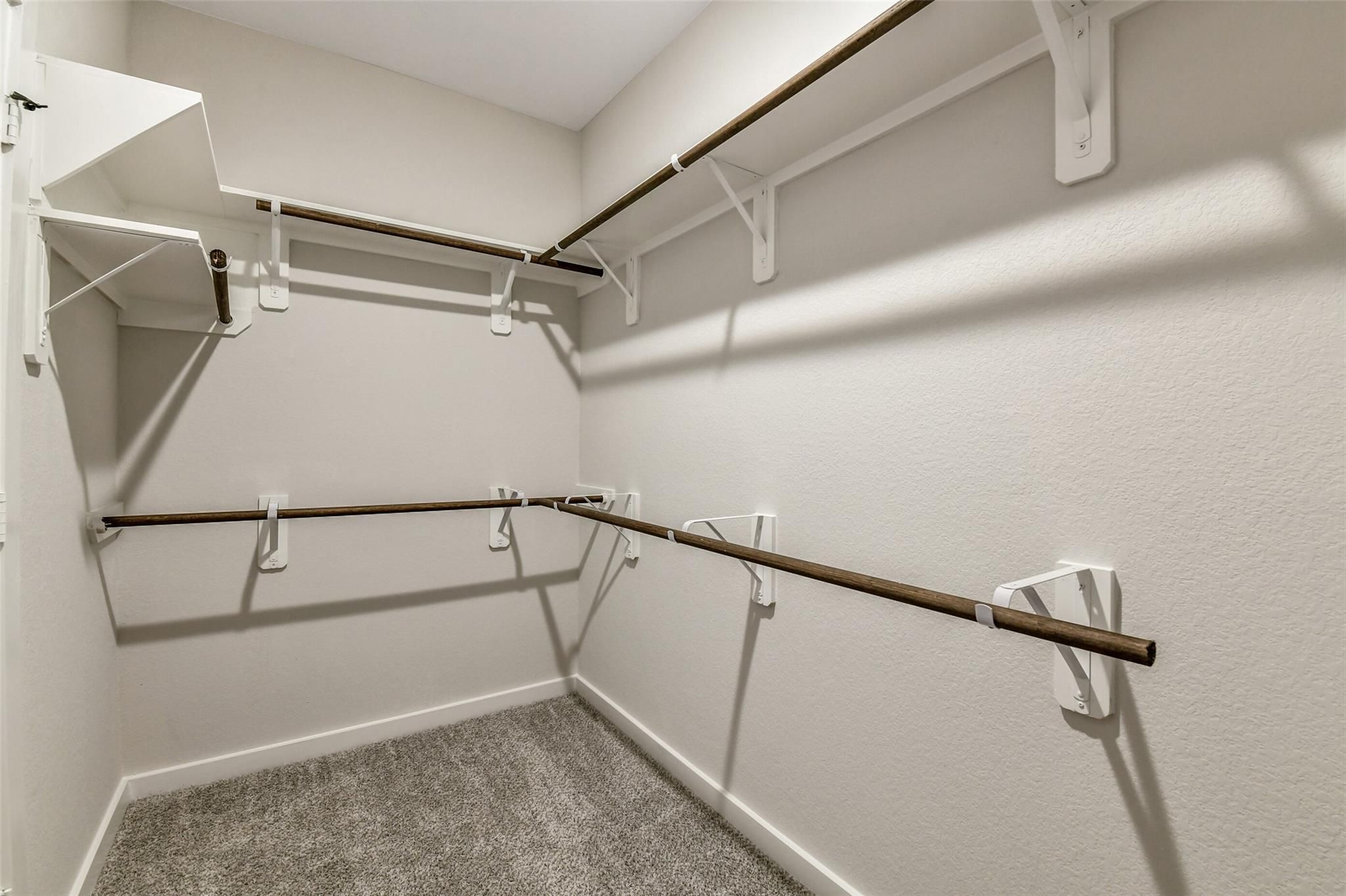 Spacious walk-in closet with wooden shelves, hanging rods, and beige walls in Davidson Homes The Daphne H, Crosby, Texas