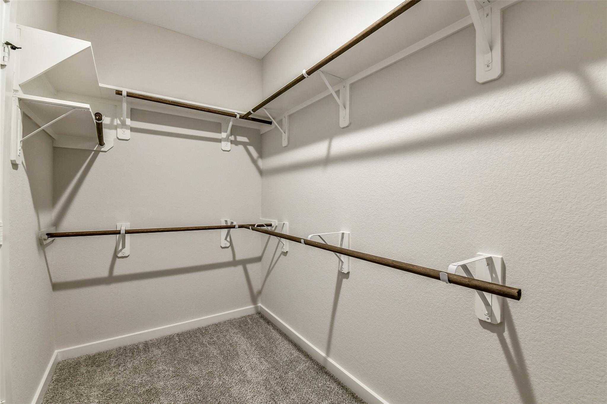 Spacious walk-in closet with wooden shelves, hanging rods, and beige walls in Davidson Homes The Daphne H, Crosby, Texas