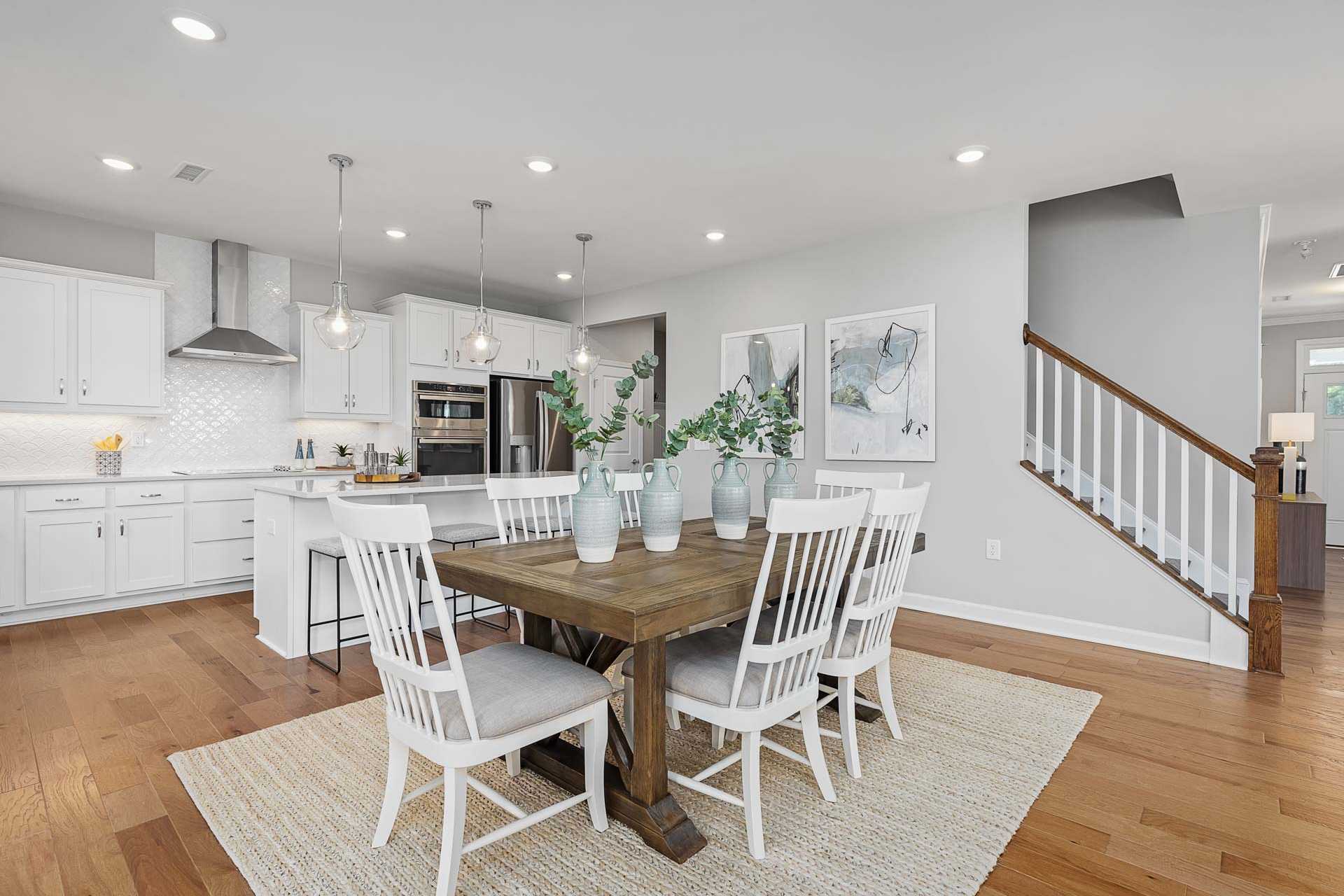 Spacious open-concept kitchen dining area in Highland Forest Fuquay-Varina NC with white cabinets farmhouse table hardwood floors pendant lights