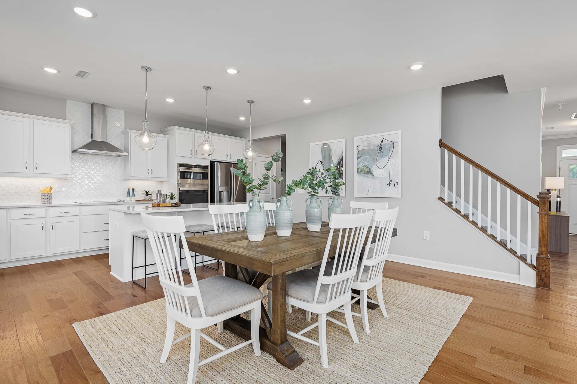 Spacious open-concept kitchen dining area in Highland Forest Fuquay-Varina NC with white cabinets farmhouse table hardwood floors pendant lights
