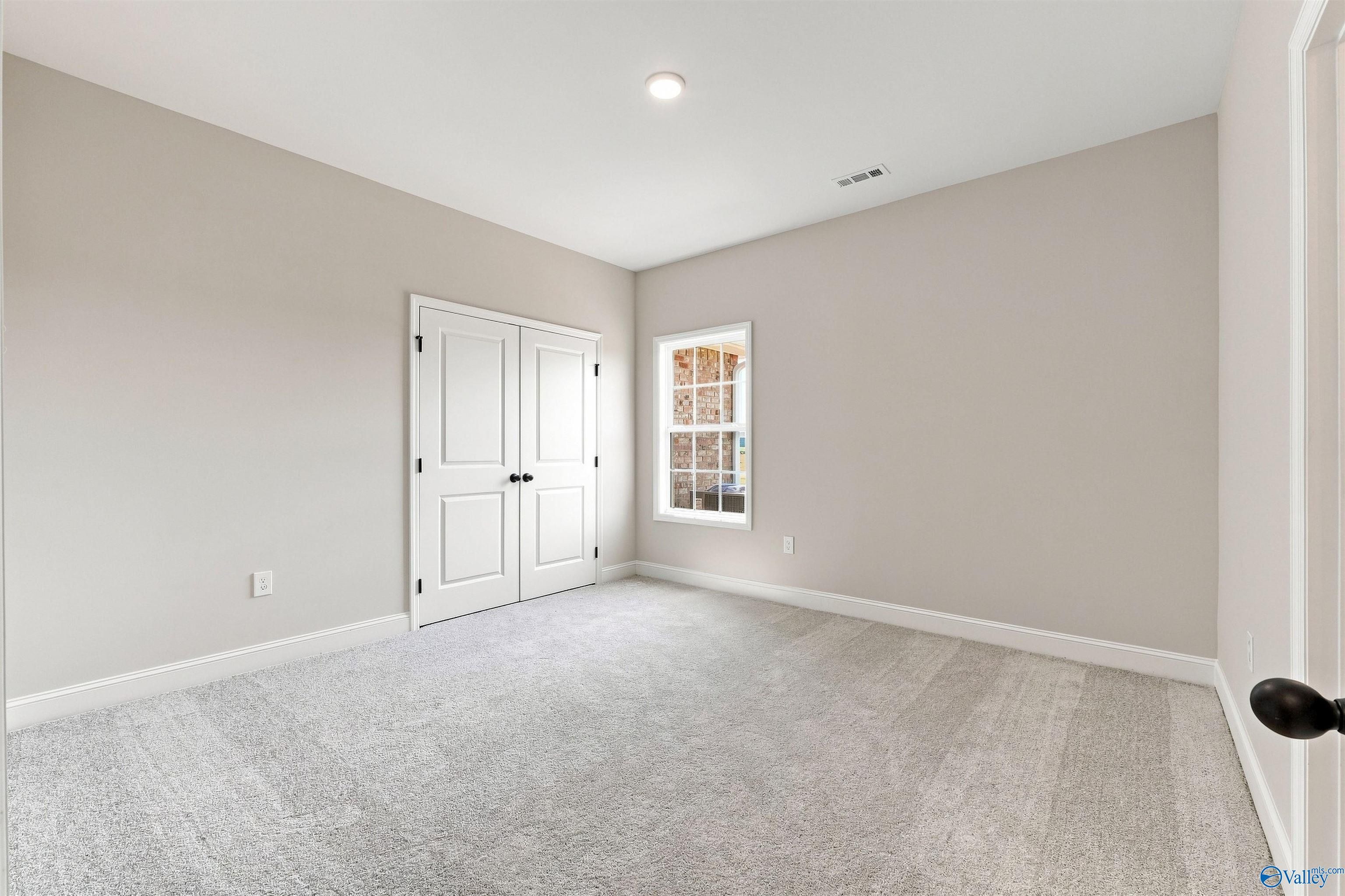 Spacious secondary bedroom with neutral carpet and double-door closet in The Oxford floor plan, Kendall Farms, Toney, AL.