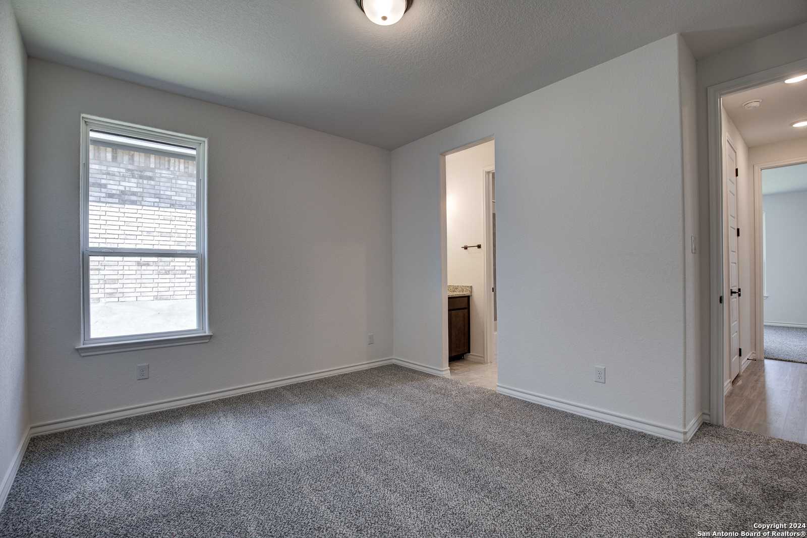 Carpeted secondary bedroom featuring en-suite bathroom vanity and large window in Davidson Homes The Garner B, Castroville, Texas