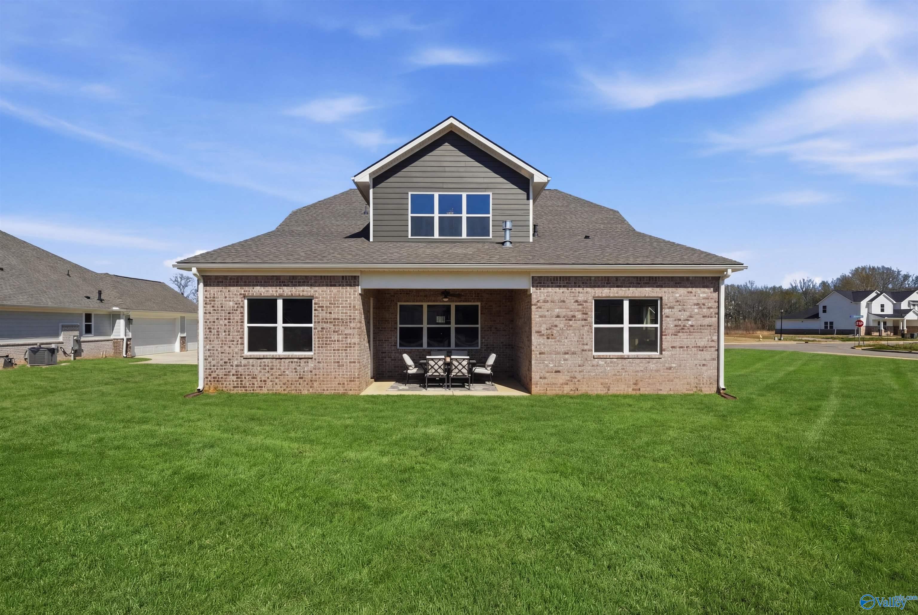 Rear view of brick and siding Oxford B home with covered patio, outdoor dining set, and lush green yard in The Meadows at Hampton Cove, Owens Cross Roads, Alabama
