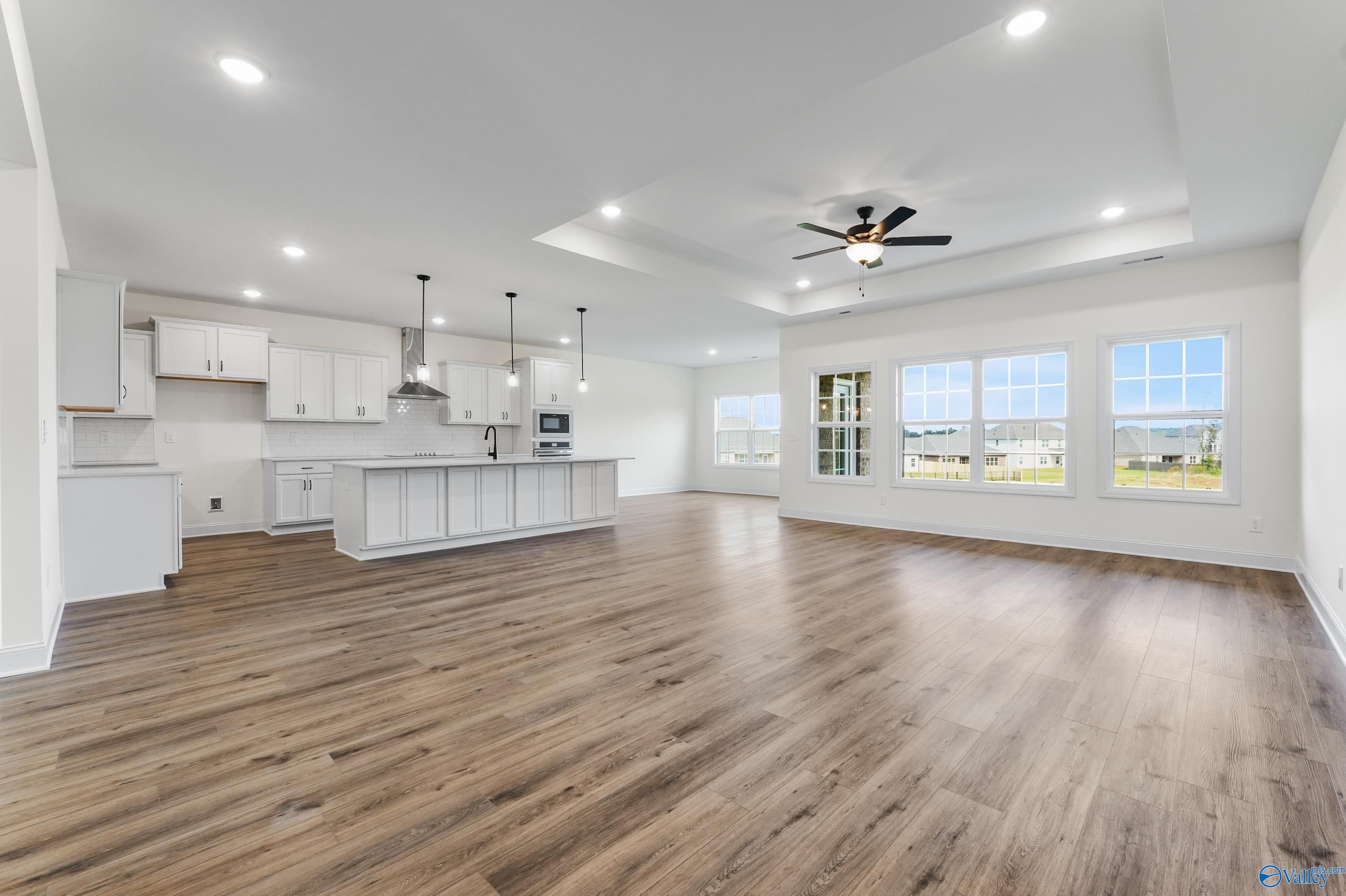 Open-concept kitchen with white cabinets, large island, pendant lights, and hardwood floors in The Finleigh by Davidson Homes, Harvest, AL
