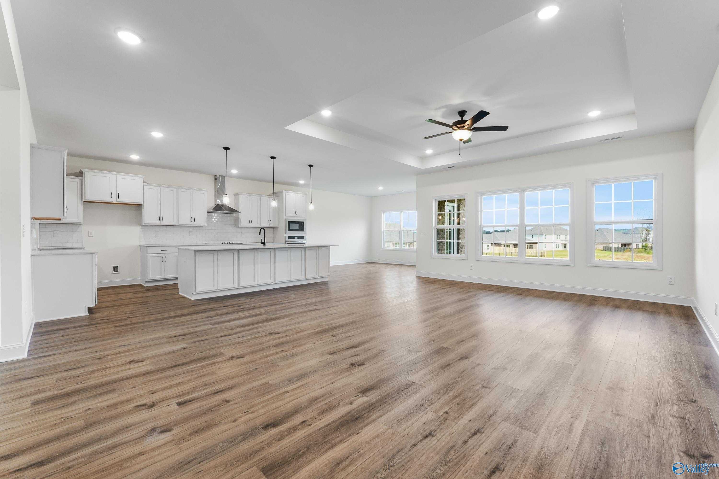 Open-concept kitchen with white cabinets, large island, pendant lights, and hardwood floors in The Finleigh by Davidson Homes, Harvest, AL