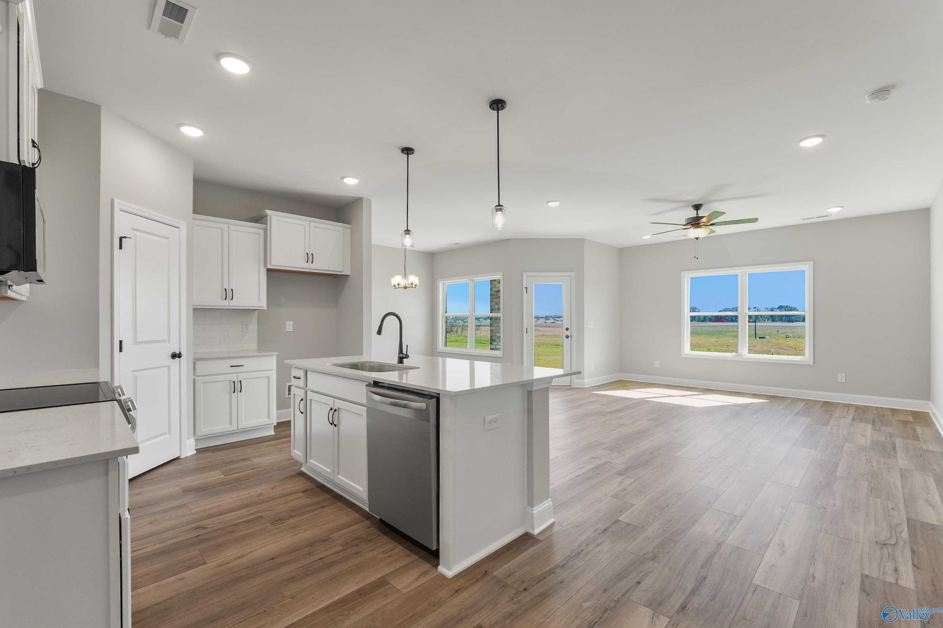 Modern open-concept kitchen with white island sink, stainless dishwasher, hardwood floors in Davidson Homes The Daphne C, Hazel Green, Alabama