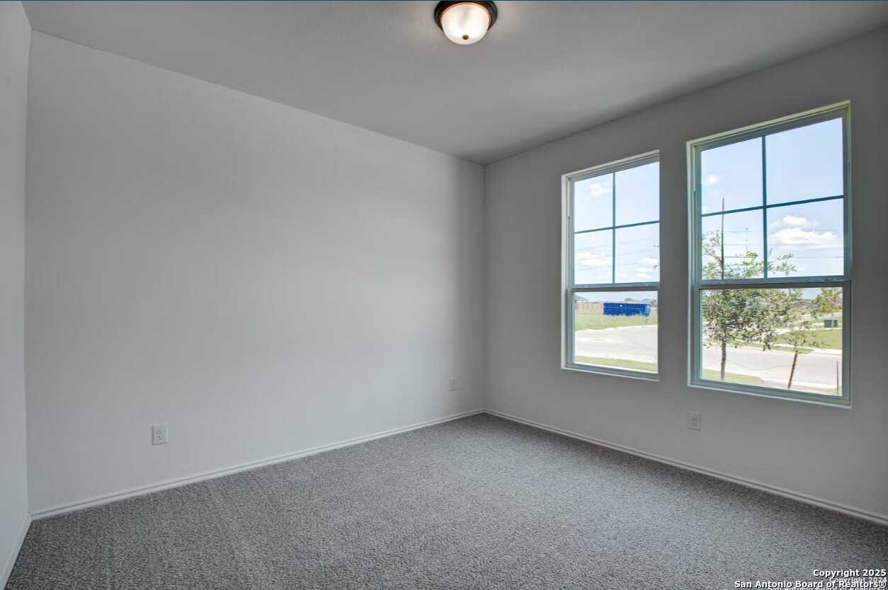 Bright empty bedroom with gray carpet, white walls, and large windows overlooking Seguin landscape in Davidson Homes The Daphne H