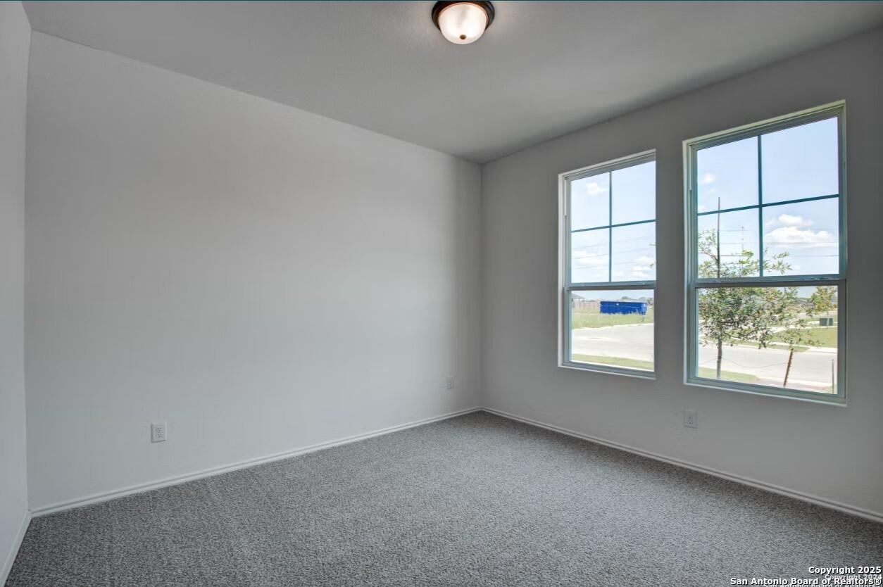 Bright empty bedroom with gray carpet, white walls, and large windows overlooking Seguin landscape in Davidson Homes The Daphne H