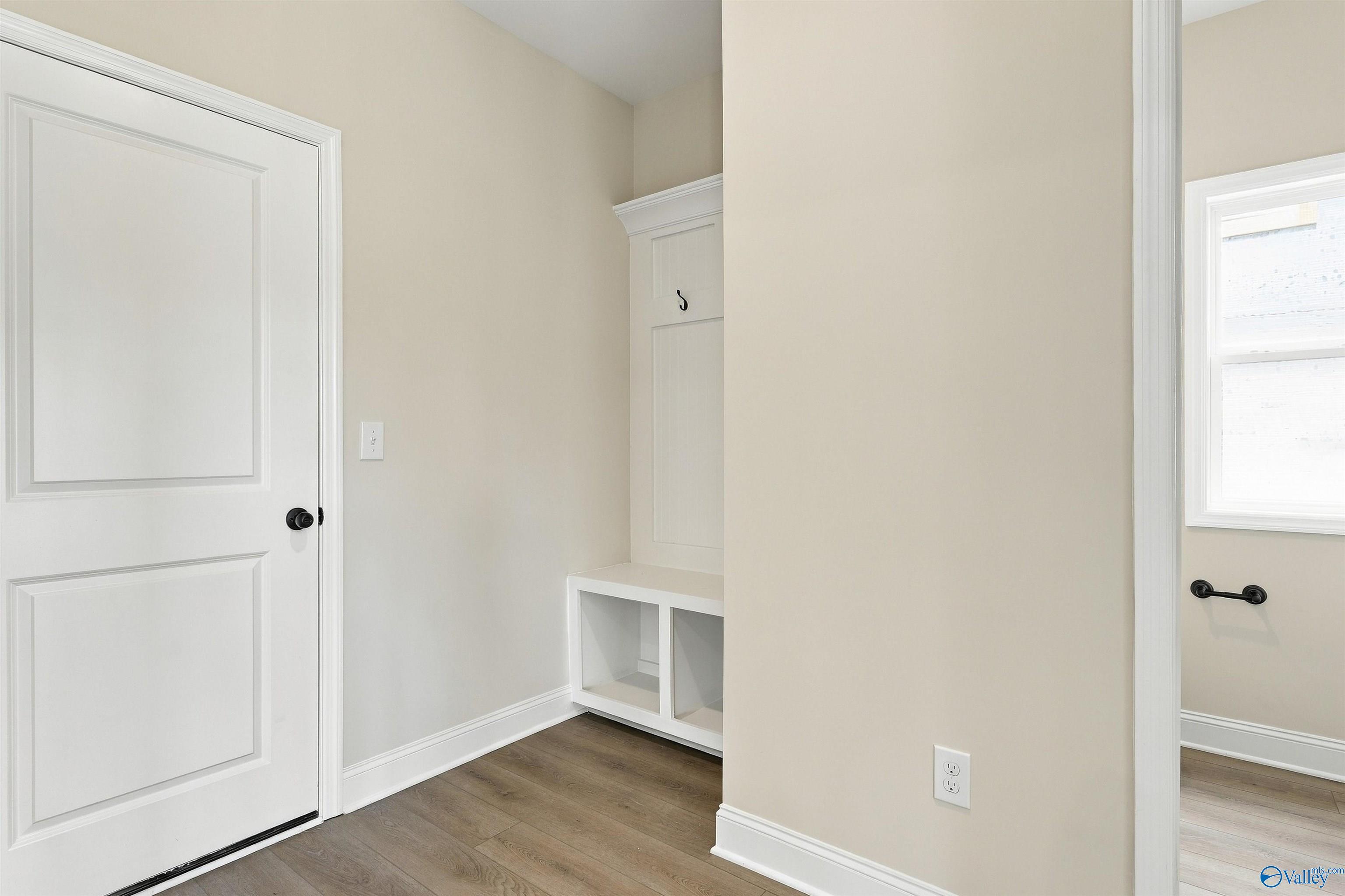 Mudroom with white built-in bench, cubbies, and coat hooks on wood-look flooring in Davidson Homes The Shelby A, Athens, Alabama