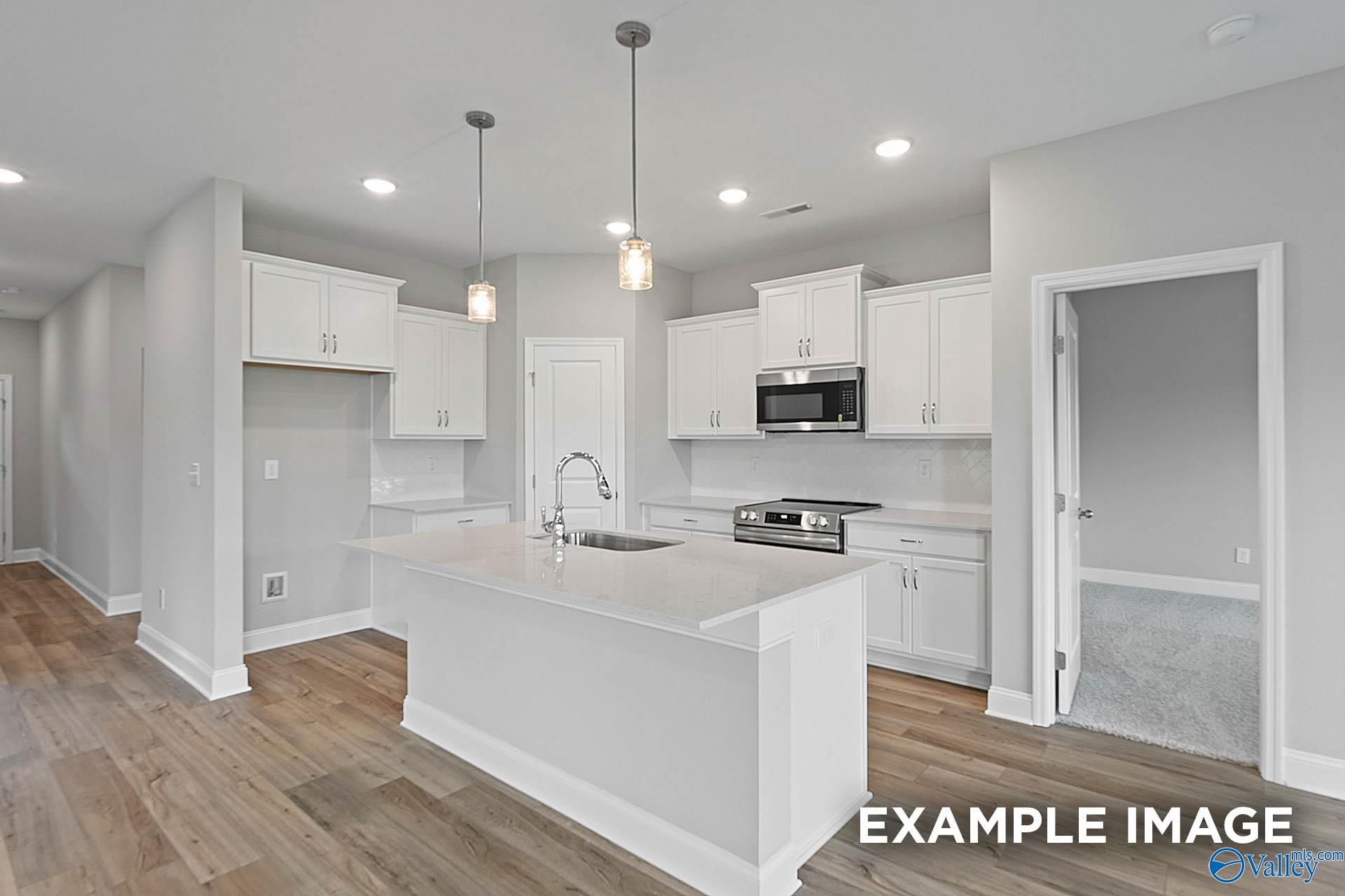 Bright open kitchen with white cabinets, large island sink, stainless microwave and oven in The Franklin E home, Hazel Green, Alabama