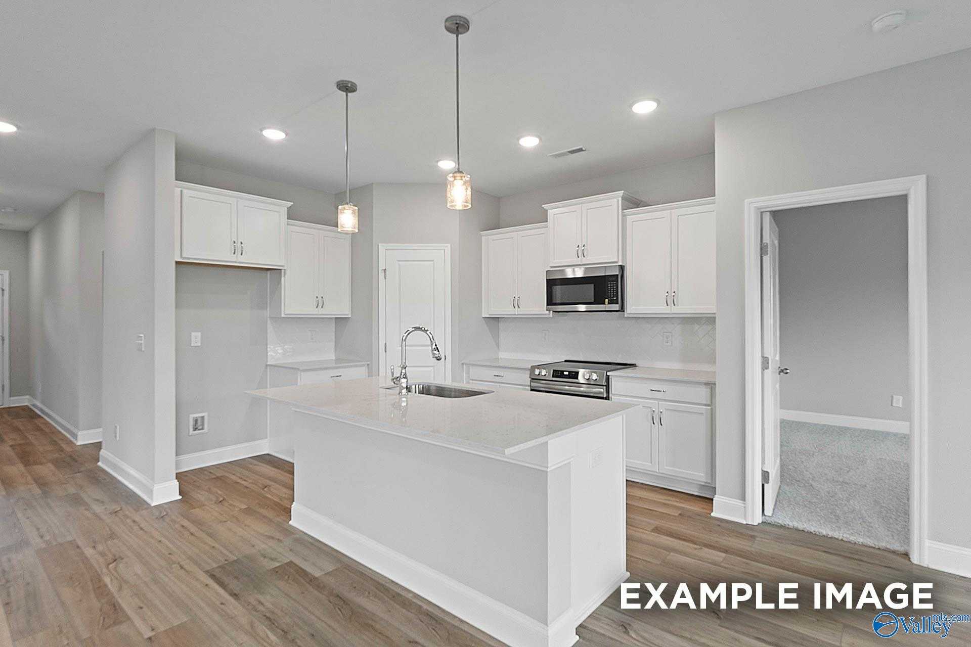 Bright open kitchen with white cabinets, large island sink, stainless microwave and oven in The Franklin E home, Hazel Green, Alabama