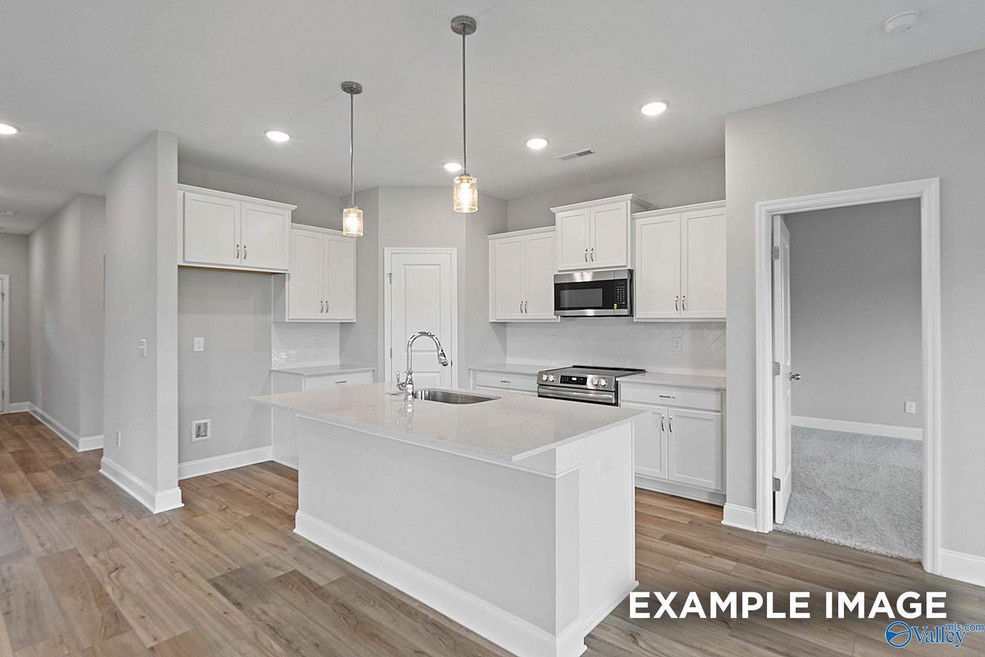 Bright open kitchen with white cabinets, large island sink, stainless microwave and oven in The Franklin E home, Hazel Green, Alabama