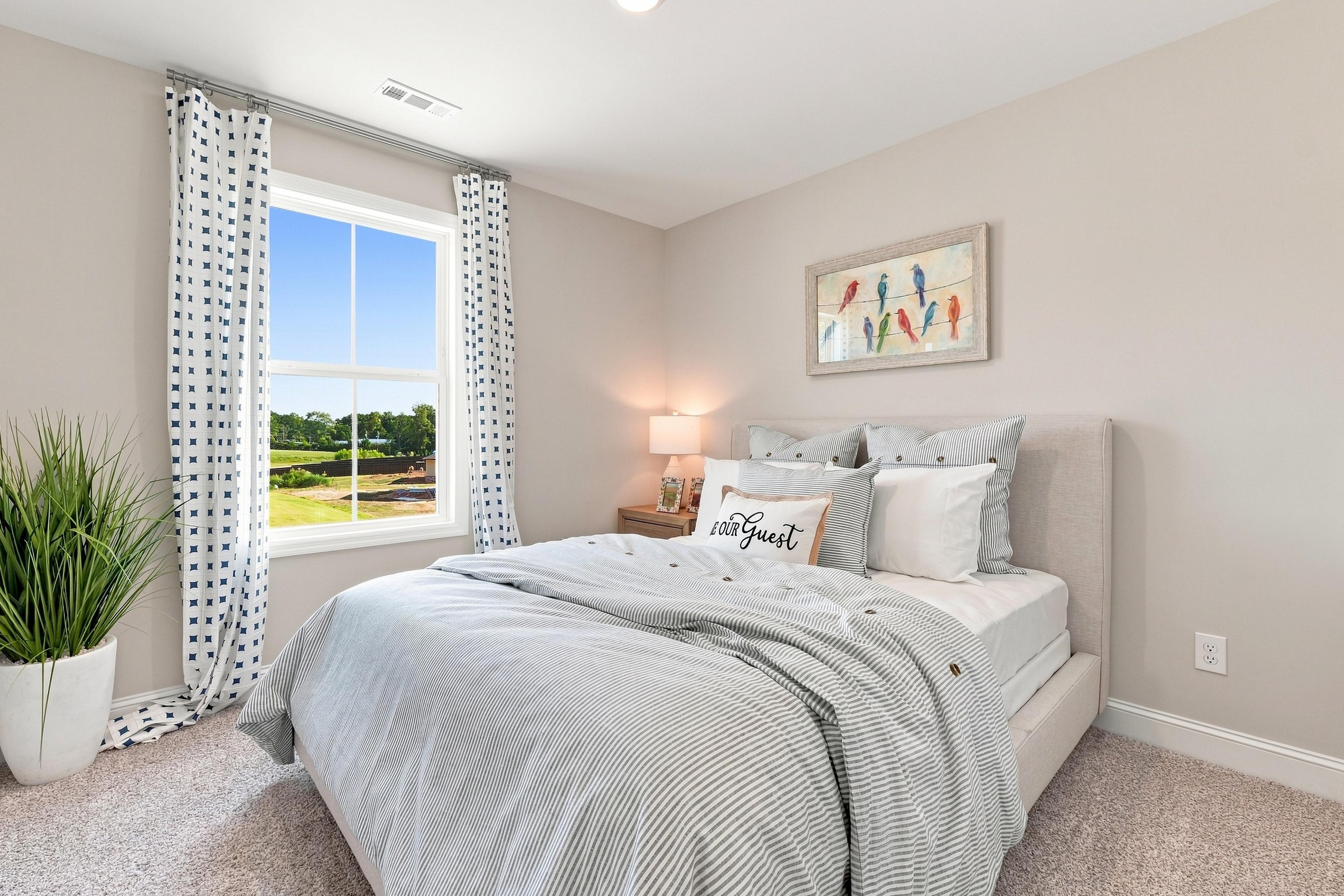 Bright guest bedroom at Bailey Park in Fayetteville, Tennessee by Davidson Homes with upholstered bed and garden view