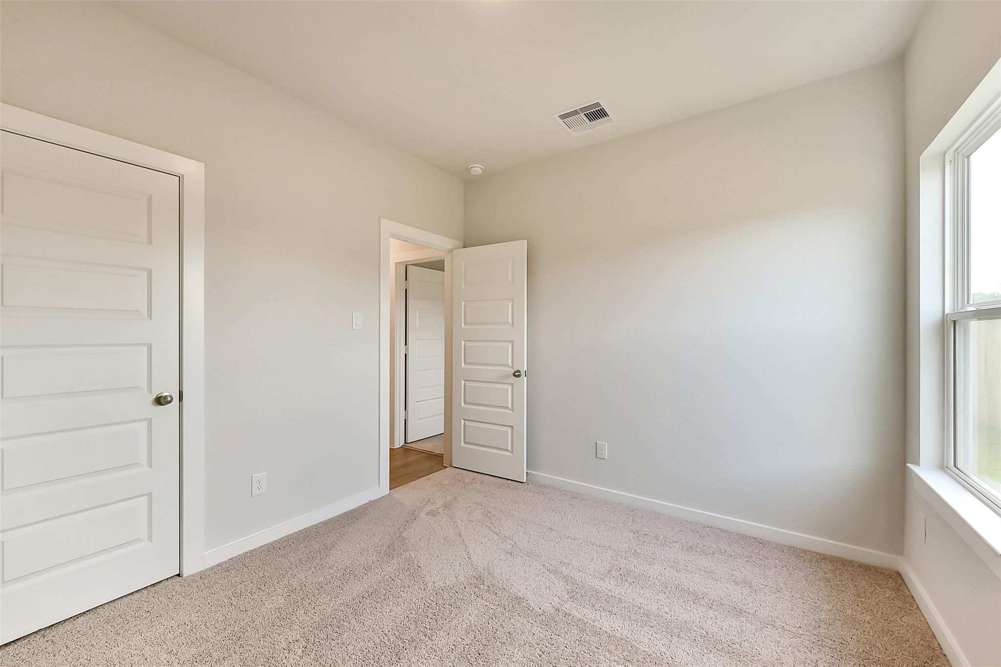 Bright secondary bedroom with beige walls, carpet floor, and window in Davidson Homes The Frio G, Dayton, Texas