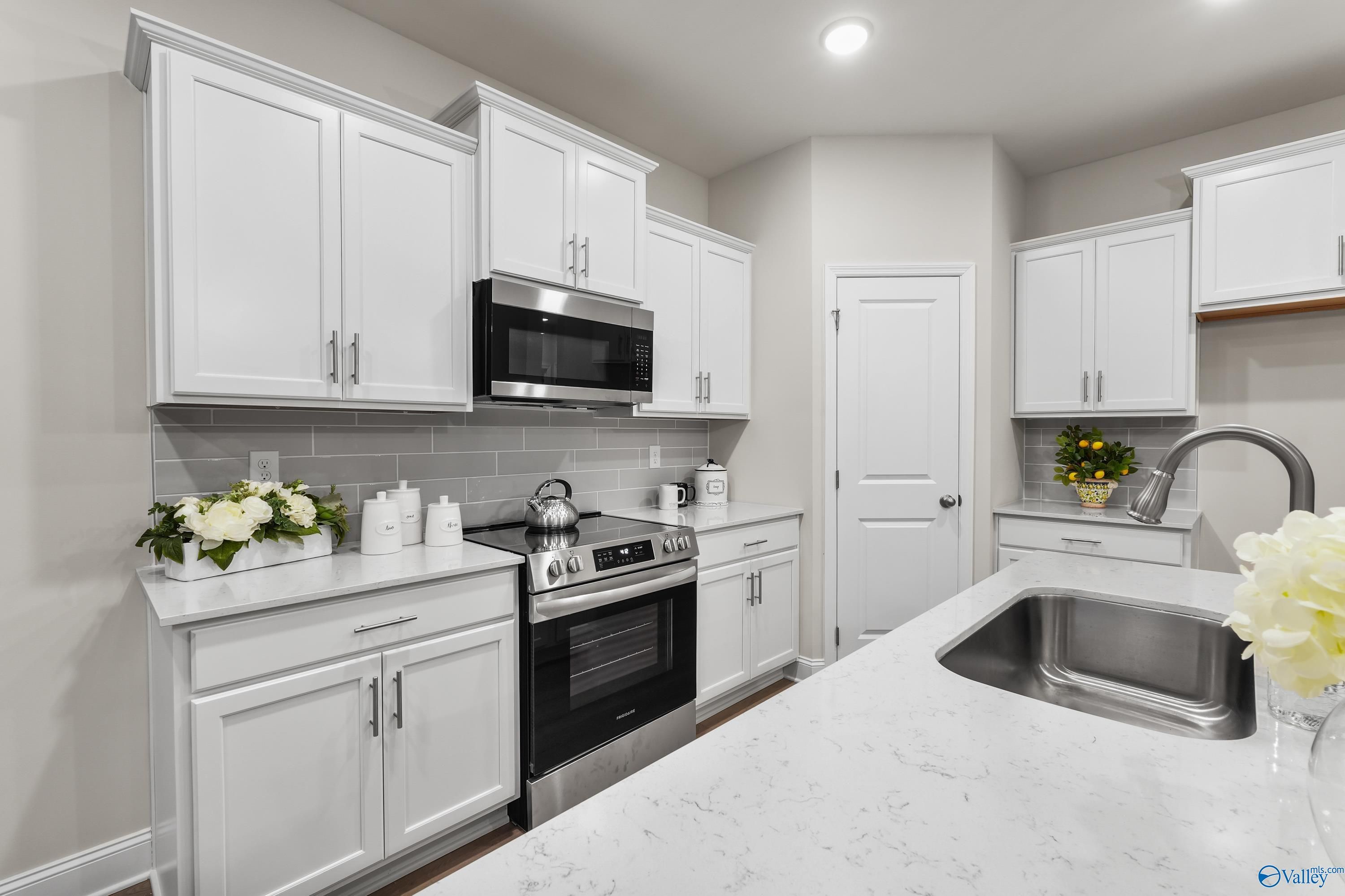 Modern kitchen featuring white shaker cabinets, stainless steel appliances, quartz countertops, and island sink in Davidson Homes The Asheville C, Huntsville, AL