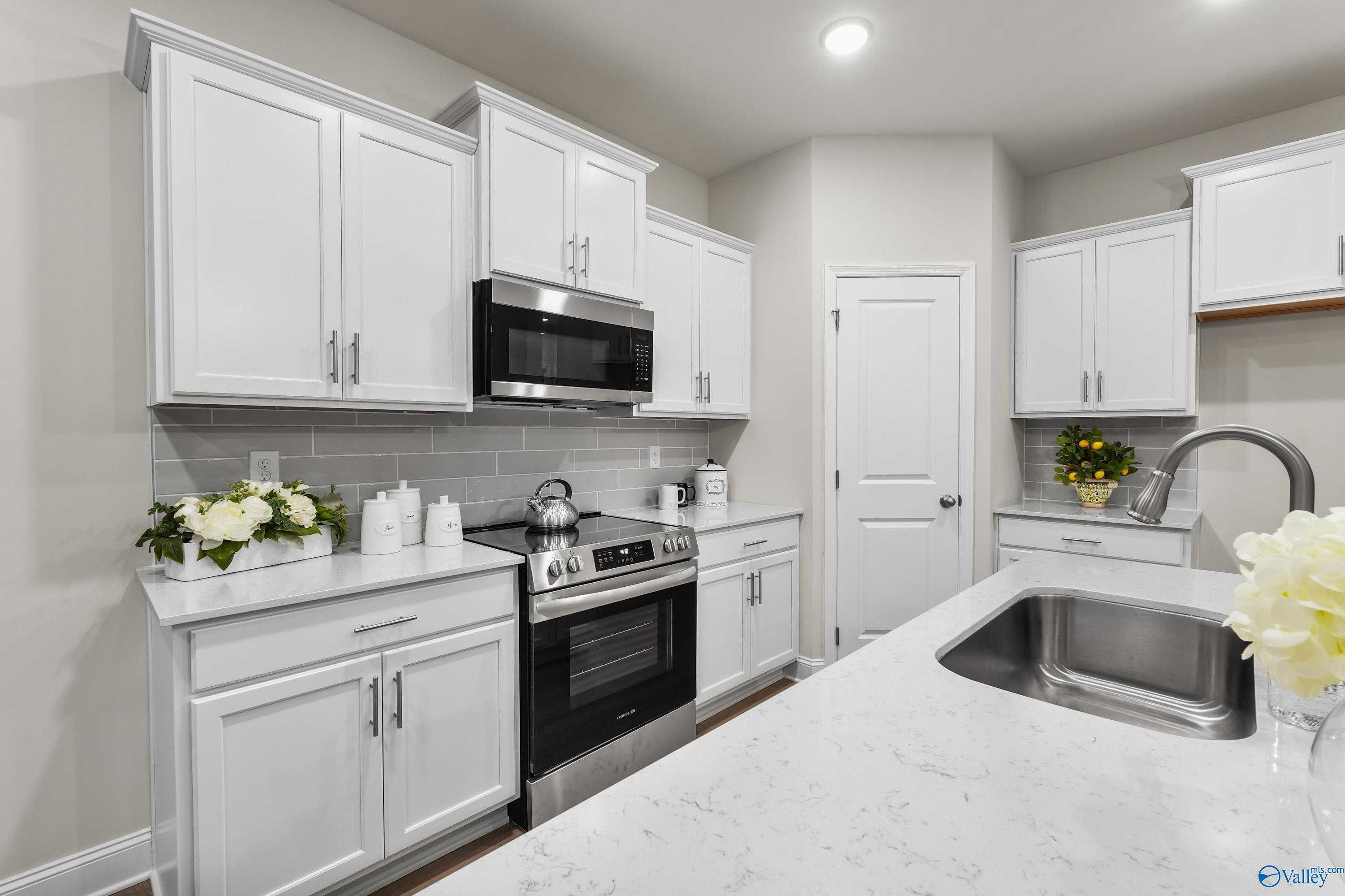 Bright modern kitchen with white shaker cabinets, quartz countertops, stainless appliances, and island sink in Davidson Homes The Asheville C, Huntsville AL