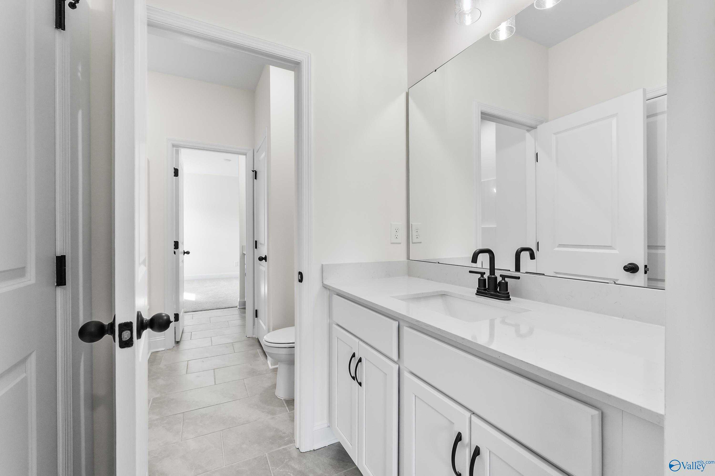 Modern guest bathroom featuring white shaker vanity, black faucet, quartz countertop, and tiled floor in Davidson Homes The Finleigh, Harvest, AL
