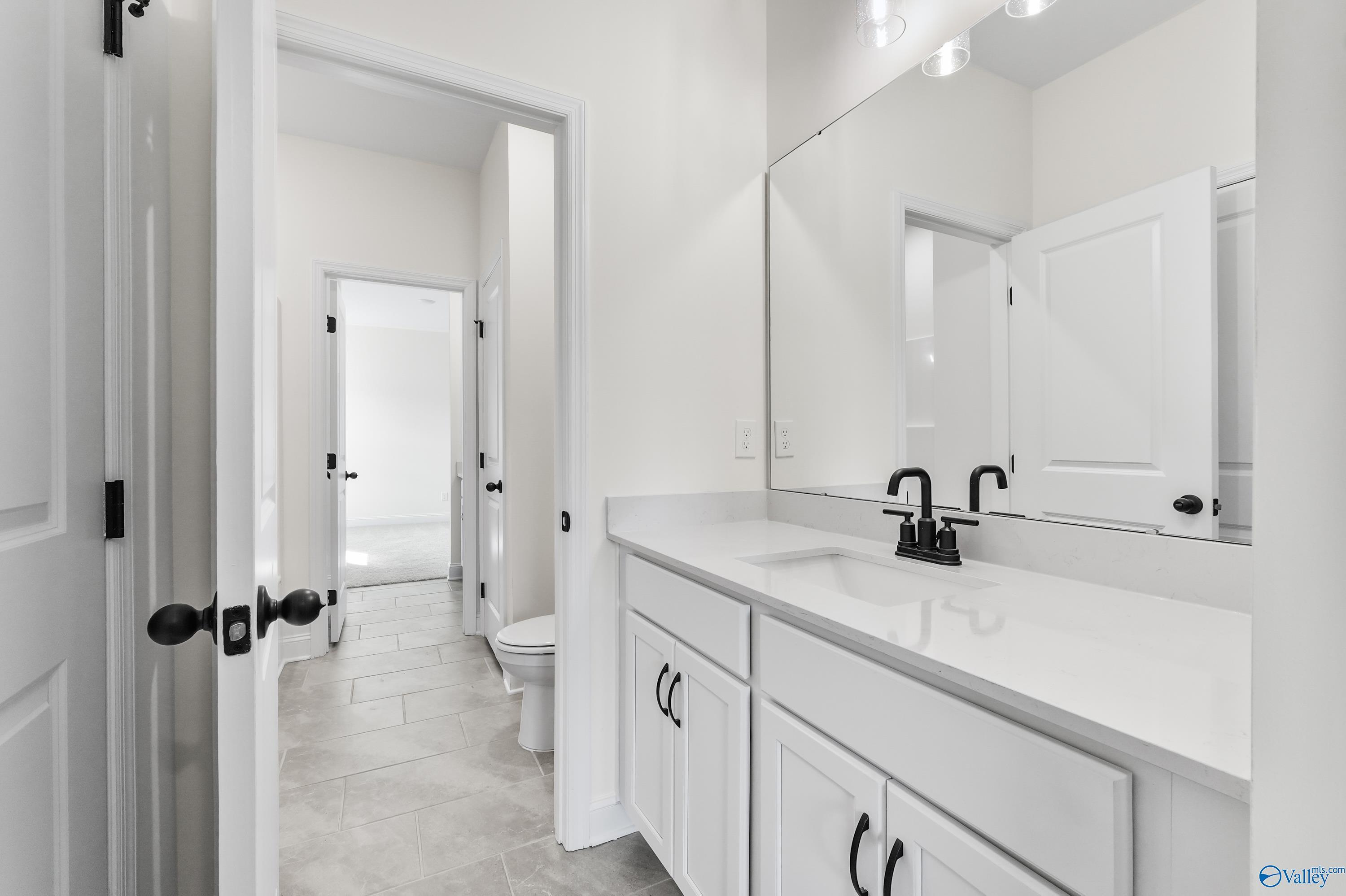 Modern guest bathroom featuring white shaker vanity, black faucet, quartz countertop, and tiled floor in Davidson Homes The Finleigh, Harvest, AL
