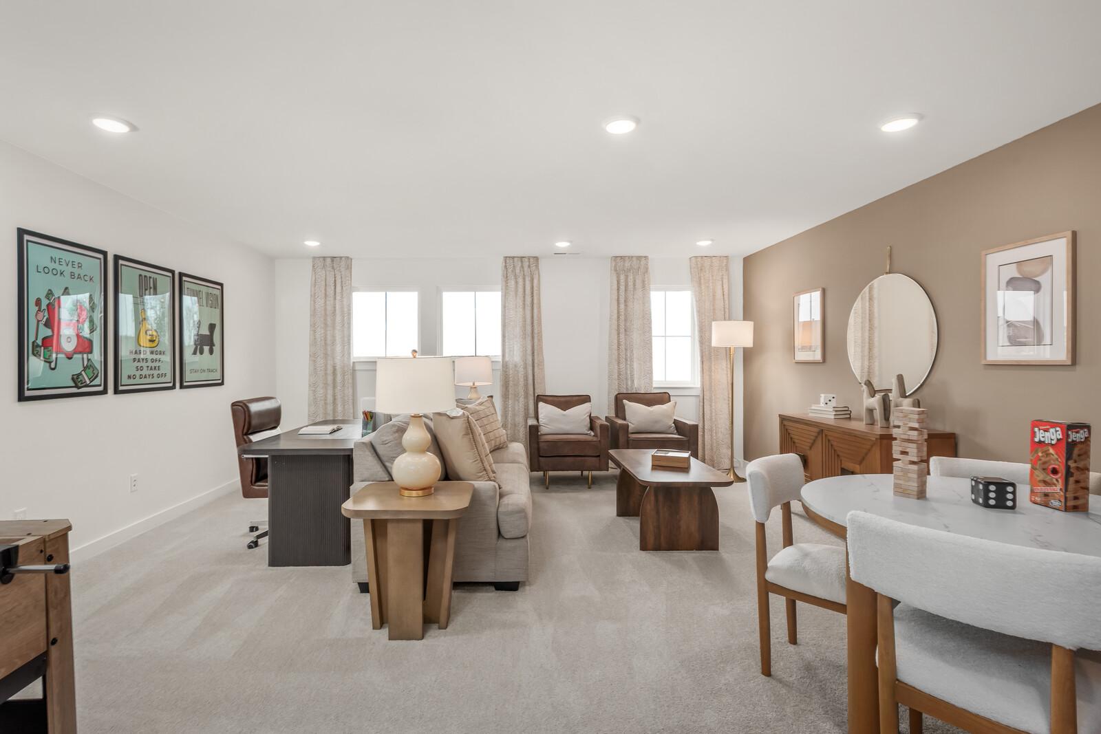 Spacious bonus room in The Ridgeport home featuring beige sofa, leather chairs, wooden desk, and modern wall art