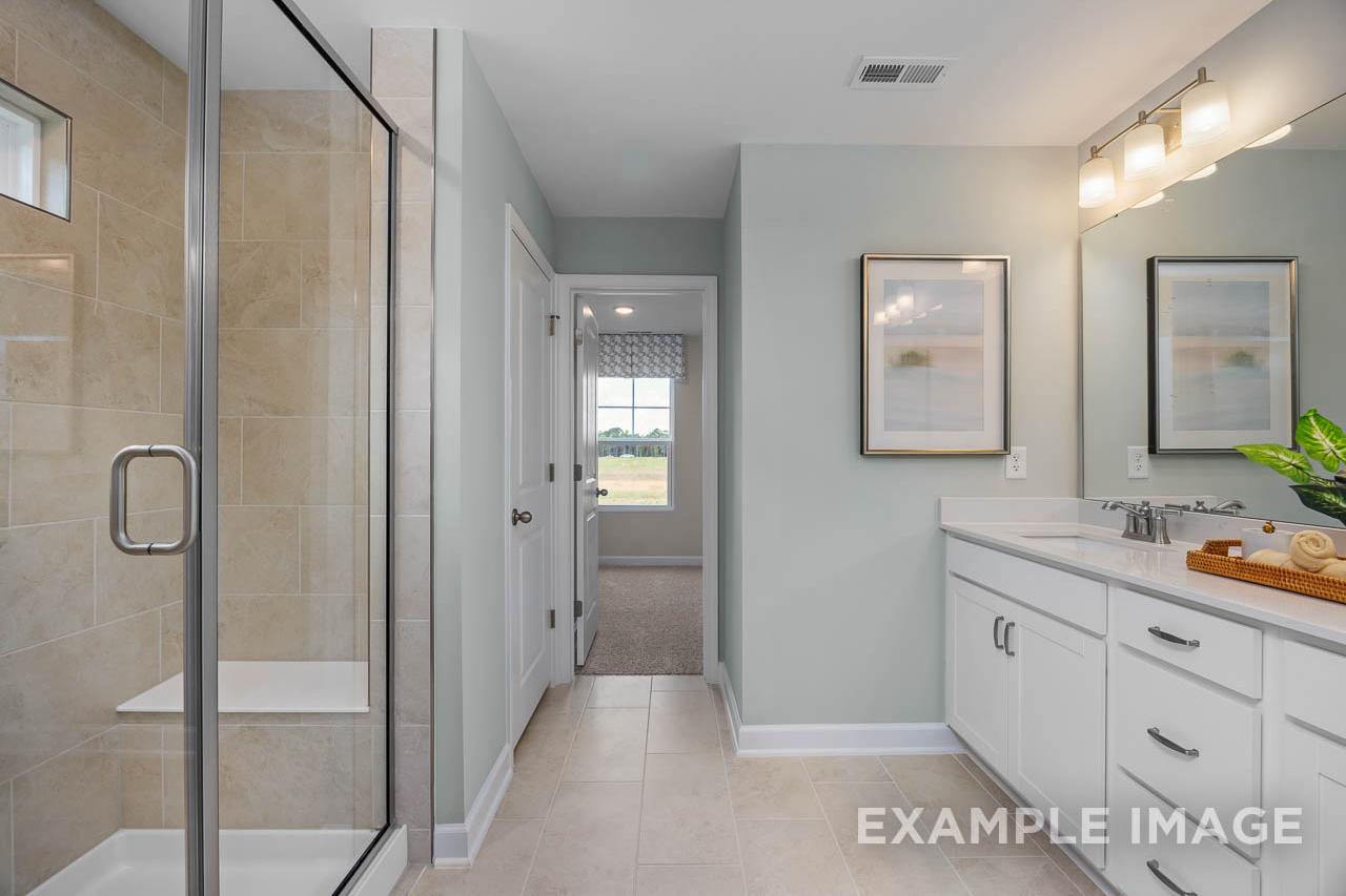 Master bathroom in The Willow by Davidson Homes featuring glass walk-in shower, white double vanity, and tile flooring