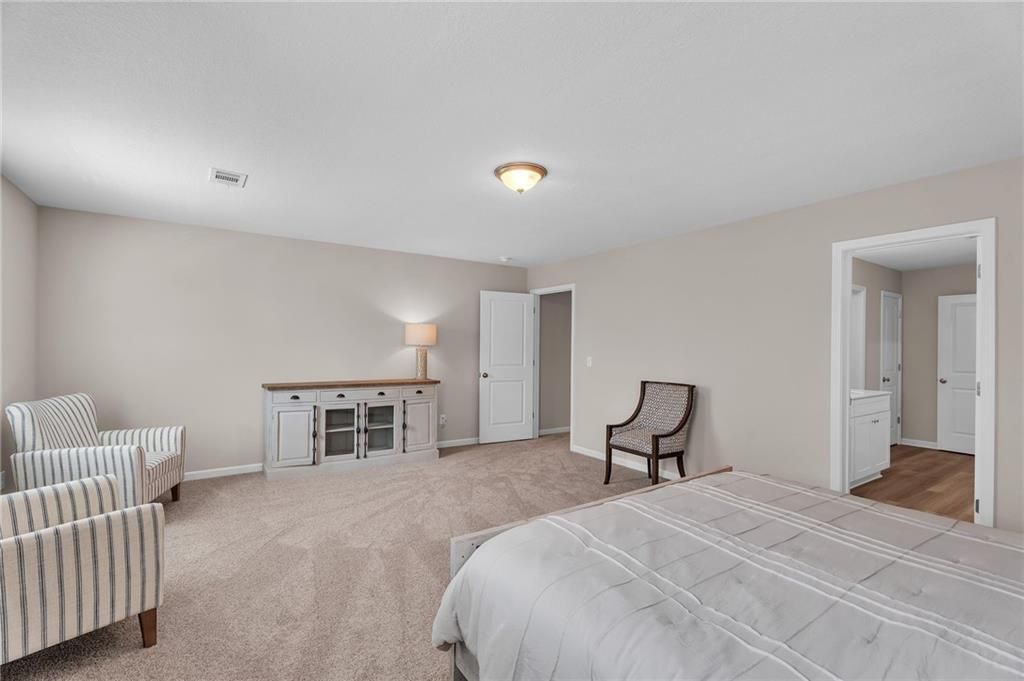 Spacious master bedroom with beige walls, king bed, striped armchairs, and walk-in closet in Davidson Homes The Bartlett, Phenix City, Alabama