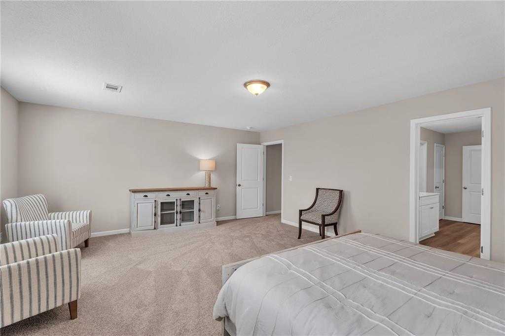 Elegant master bedroom with king bed, striped armchairs, wooden credenza, and en-suite bath in Davidson Homes The Bartlett, Phenix City