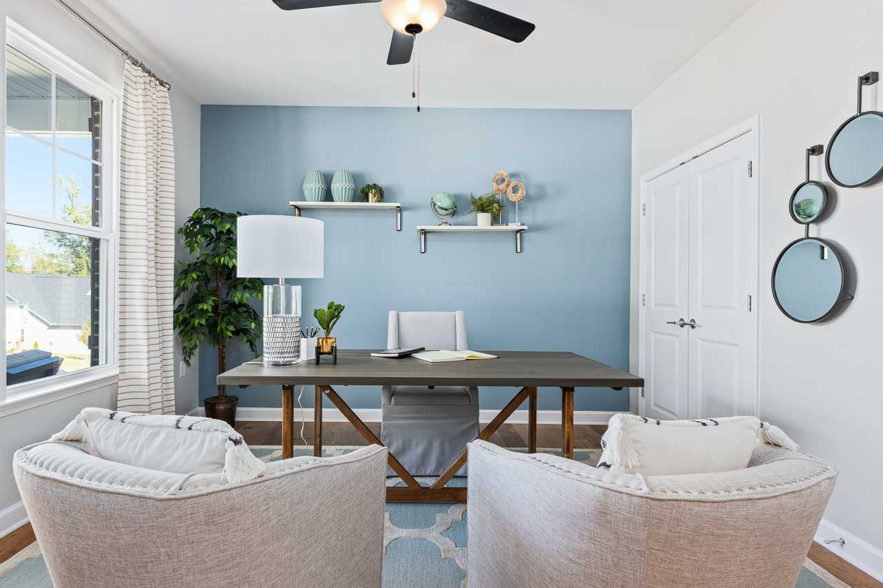 Cozy home office in Prince Place, Fuquay-Varina NC with wooden desk, blue accent wall, potted plants, ceiling fan and lounge chairs
