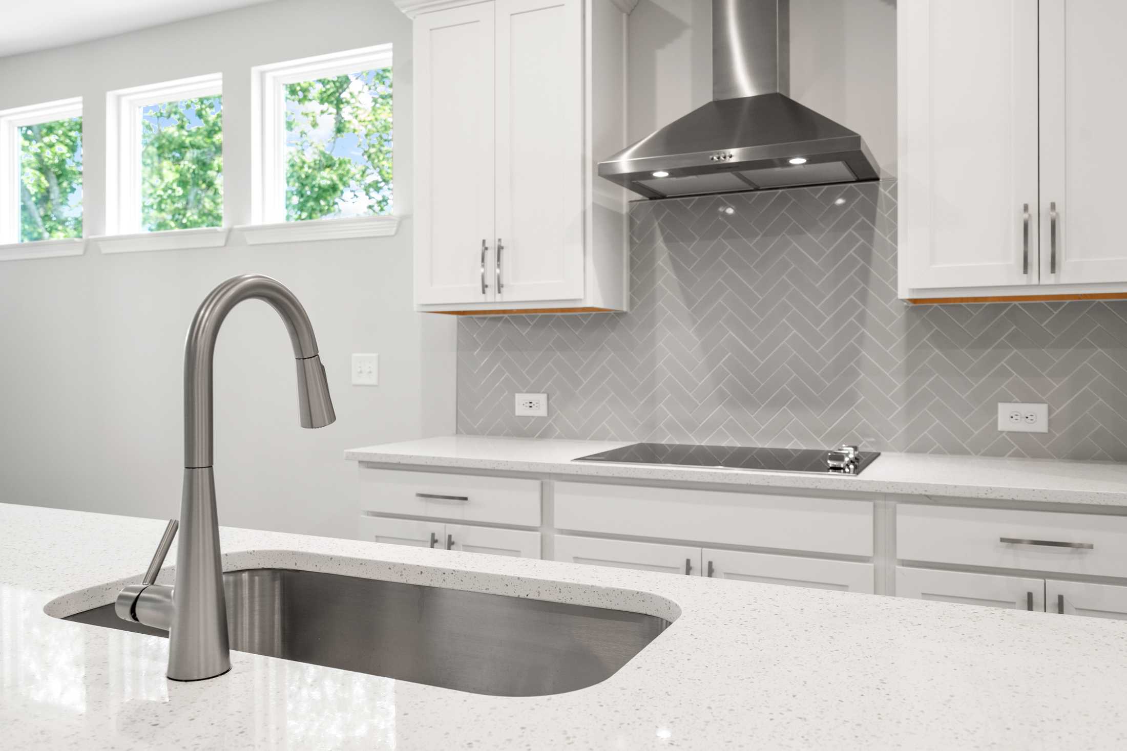 Spacious modern kitchen in The Ash B featuring white shaker cabinets, stainless steel farmhouse sink, range, and gray herringbone backsplash