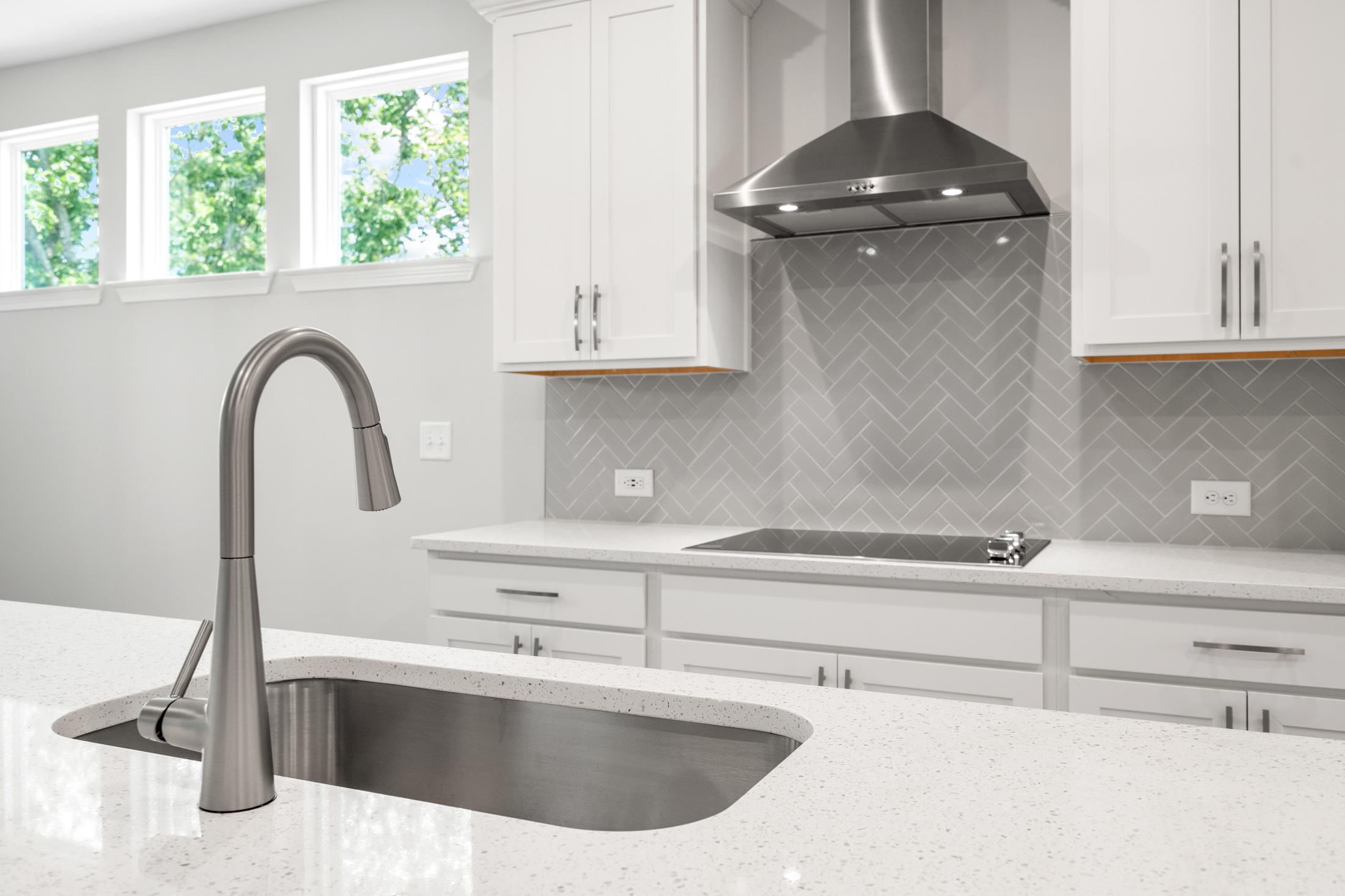Spacious modern kitchen in The Ash B featuring white shaker cabinets, stainless steel farmhouse sink, range, and gray herringbone backsplash