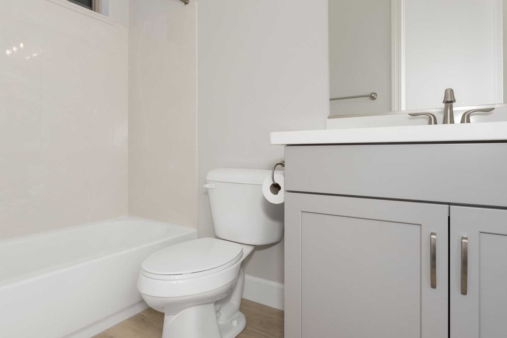 Spacious bathroom in The Daybreak C with white bathtub, toilet, gray vanity, sink, and mirror