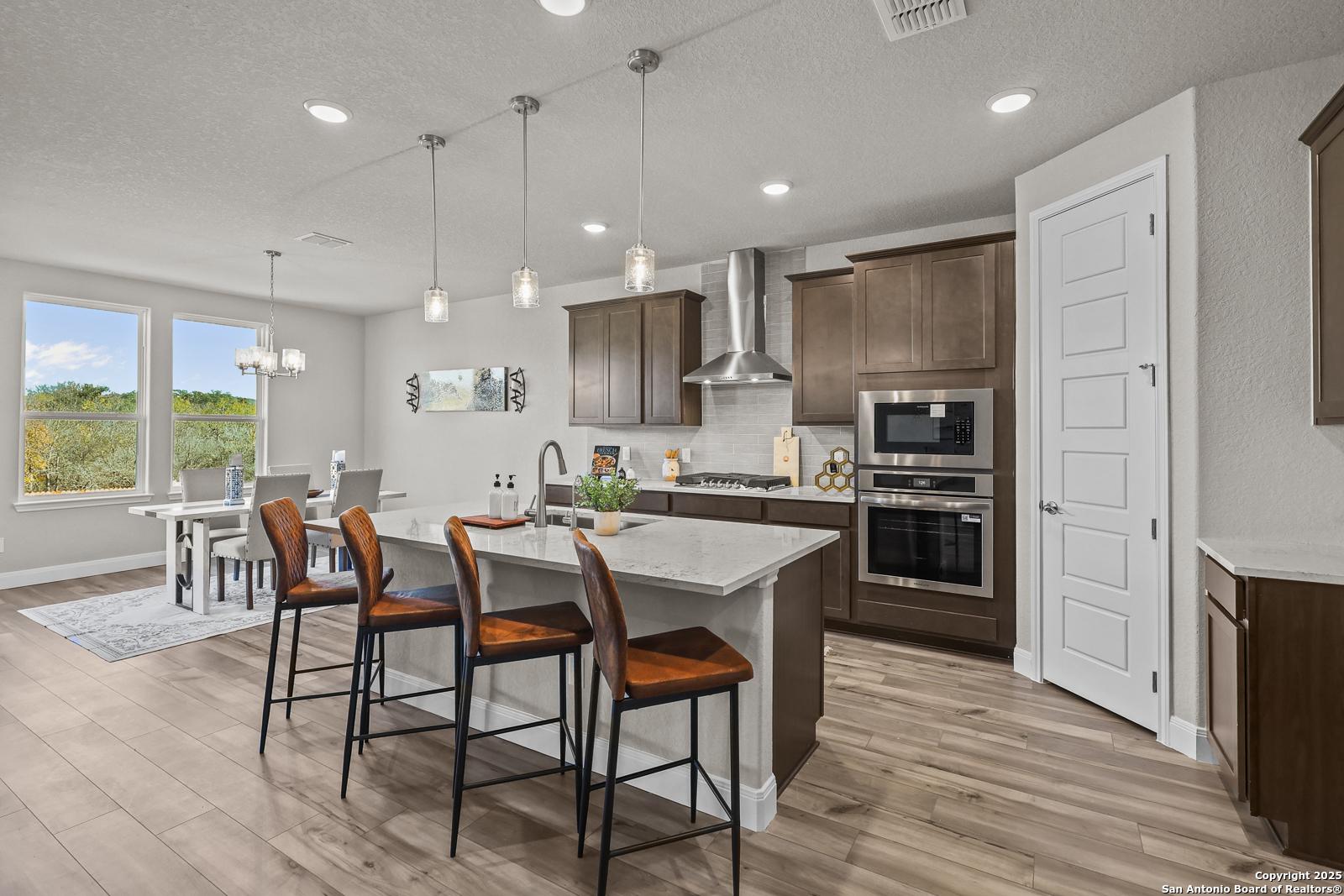 Modern open-concept kitchen with dark cabinets, white island, stainless appliances, and dining area in The Jennings G, Castroville, Texas