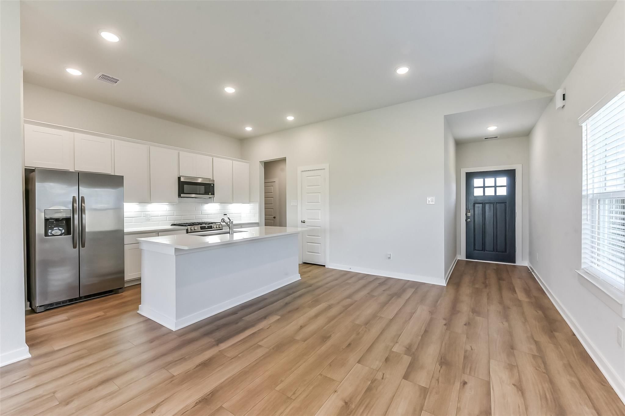 Modern white kitchen with stainless steel fridge, quartz island, subway tile backsplash, and open entry in Davidson Homes Costa B, Dayton TX