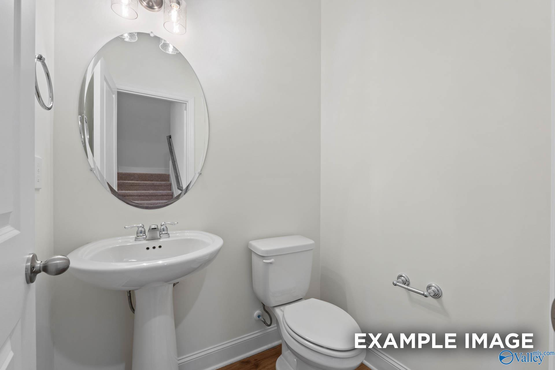 Elegant powder room with pedestal sink, round lighted mirror, and toilet in Davidson Homes The Rockford B, Athens, Alabama