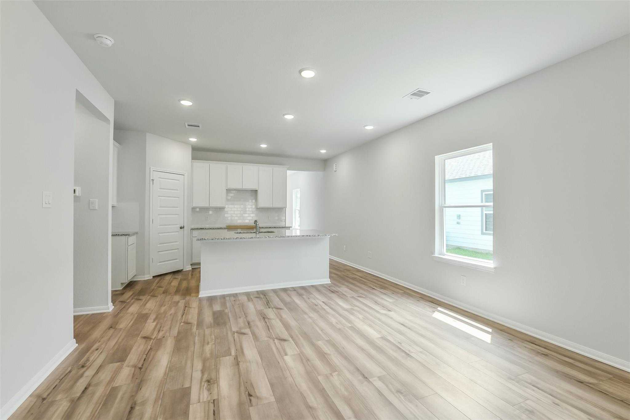 Spacious open kitchen with white cabinets, large island, and hardwood floors in Davidson Homes The Sabine E, Conroe Texas