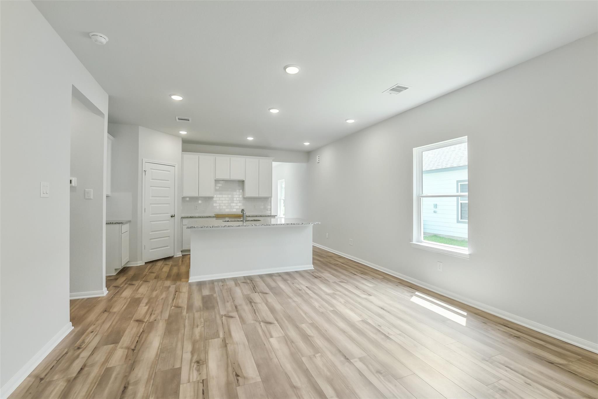 Spacious open kitchen with white cabinets, large island, and hardwood floors in Davidson Homes The Sabine E, Conroe Texas