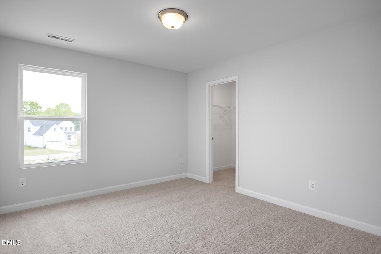 Bright secondary bedroom with light gray walls, neutral carpet, and open closet in 5-bedroom Hickory II B home, Zebulon, NC