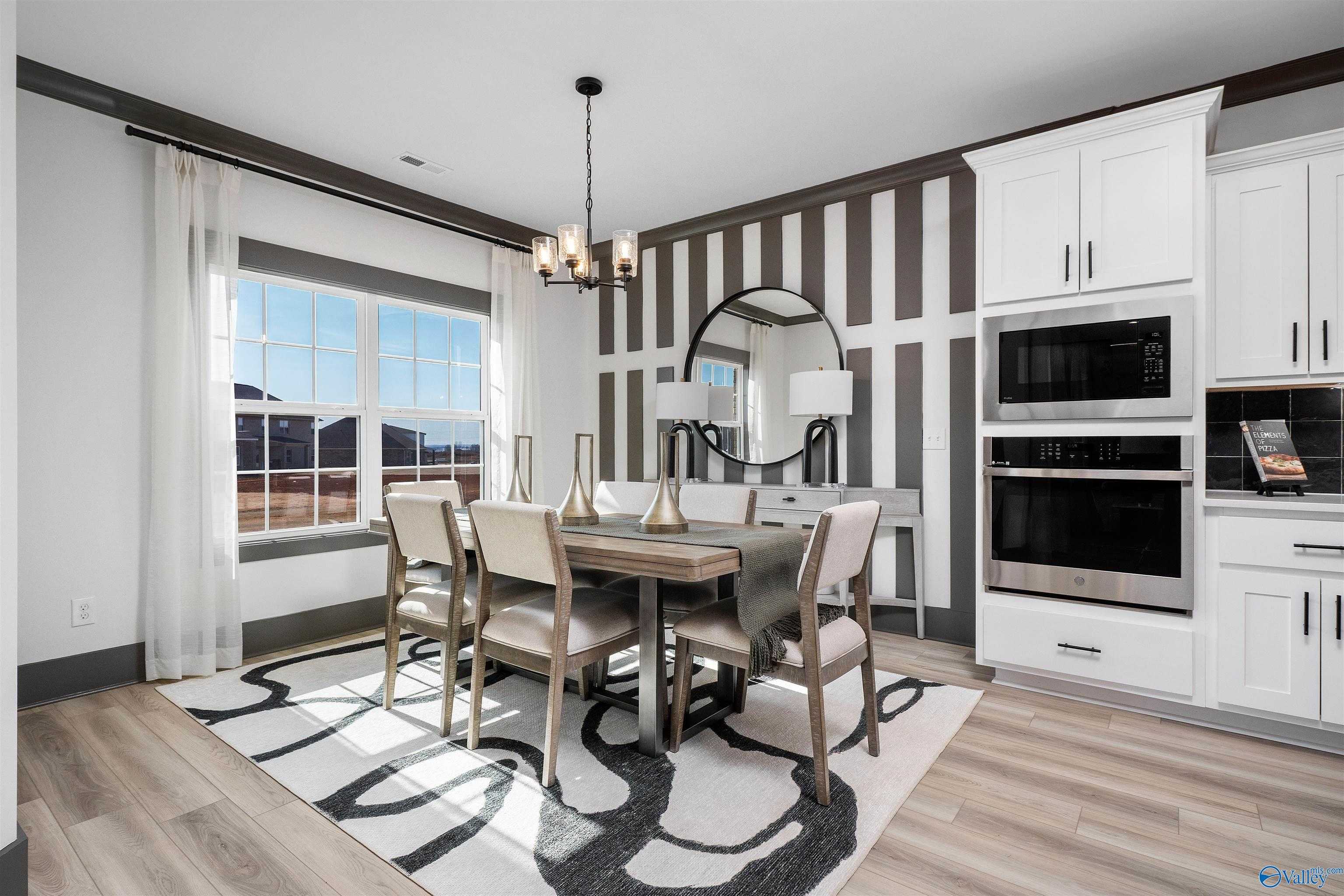 Elegant dining room with wooden table, beige chairs, chandelier, and striped wall open to white kitchen in Davidson Homes The Rockford B, Madison, AL