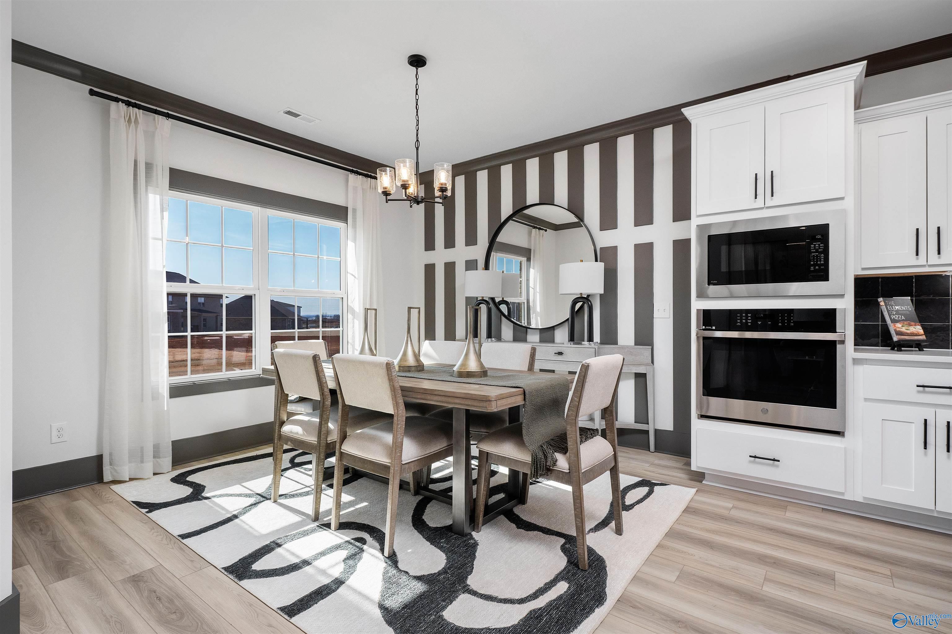 Elegant dining room with striped walls, chandelier, round mirror & wooden table in The Rockford B by Davidson Homes, Madison, Alabama