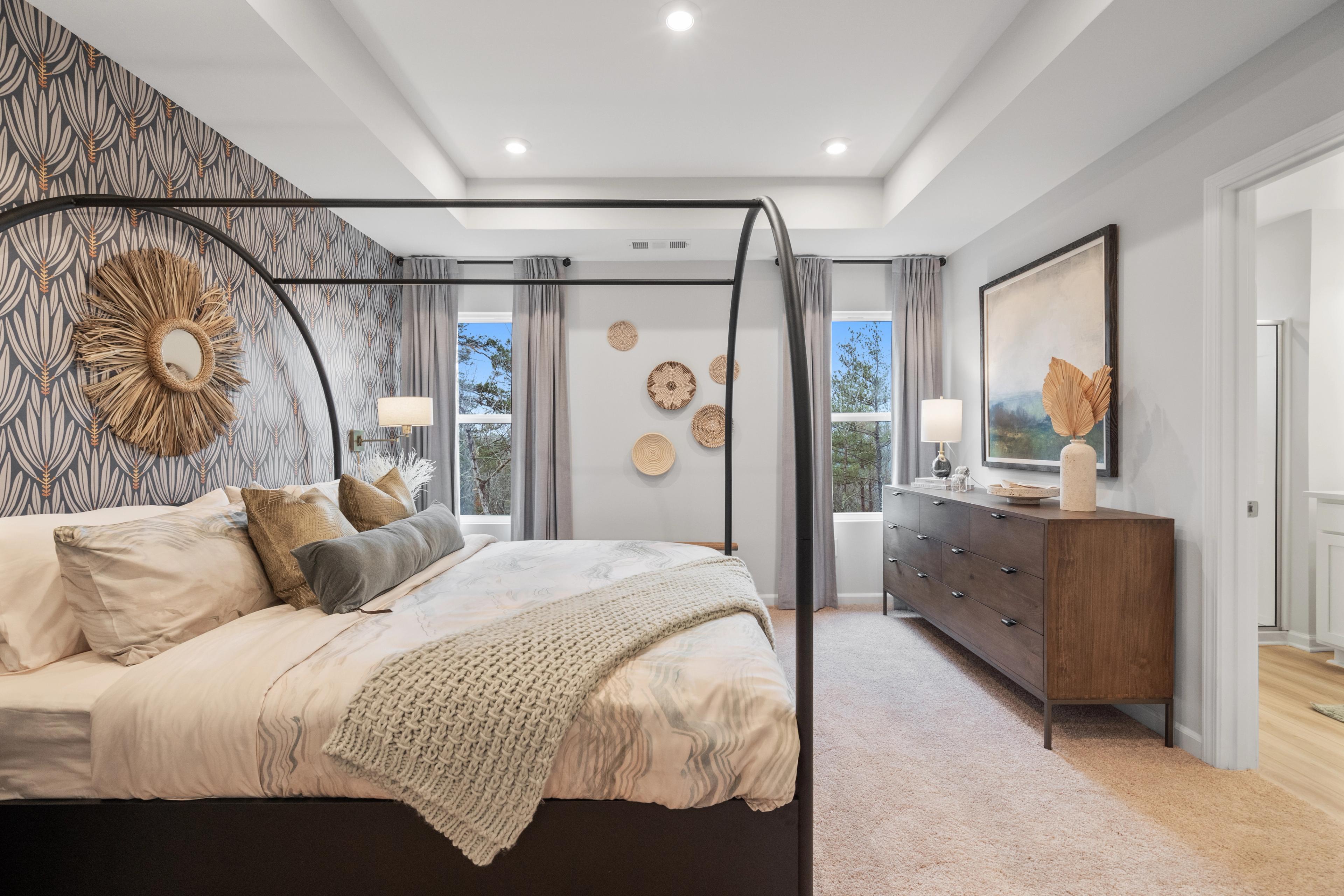 Spacious master bedroom in Stegall Village, Emerson GA with canopy bed, leaf-patterned wallpaper, and woven wall art by Davidson Homes