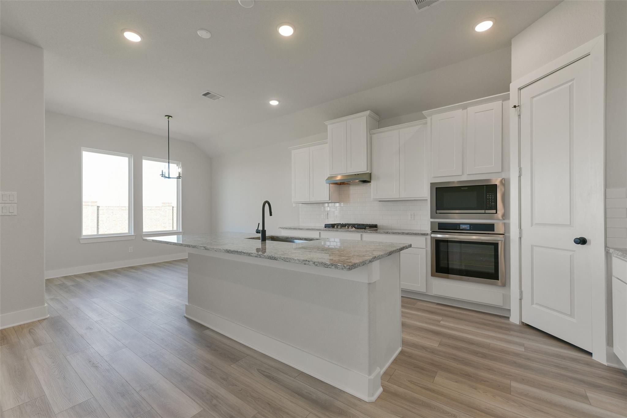 Modern white kitchen with granite island, stainless double ovens, open to living area in Davidson Homes The Edward C, Lago Mar, Texas