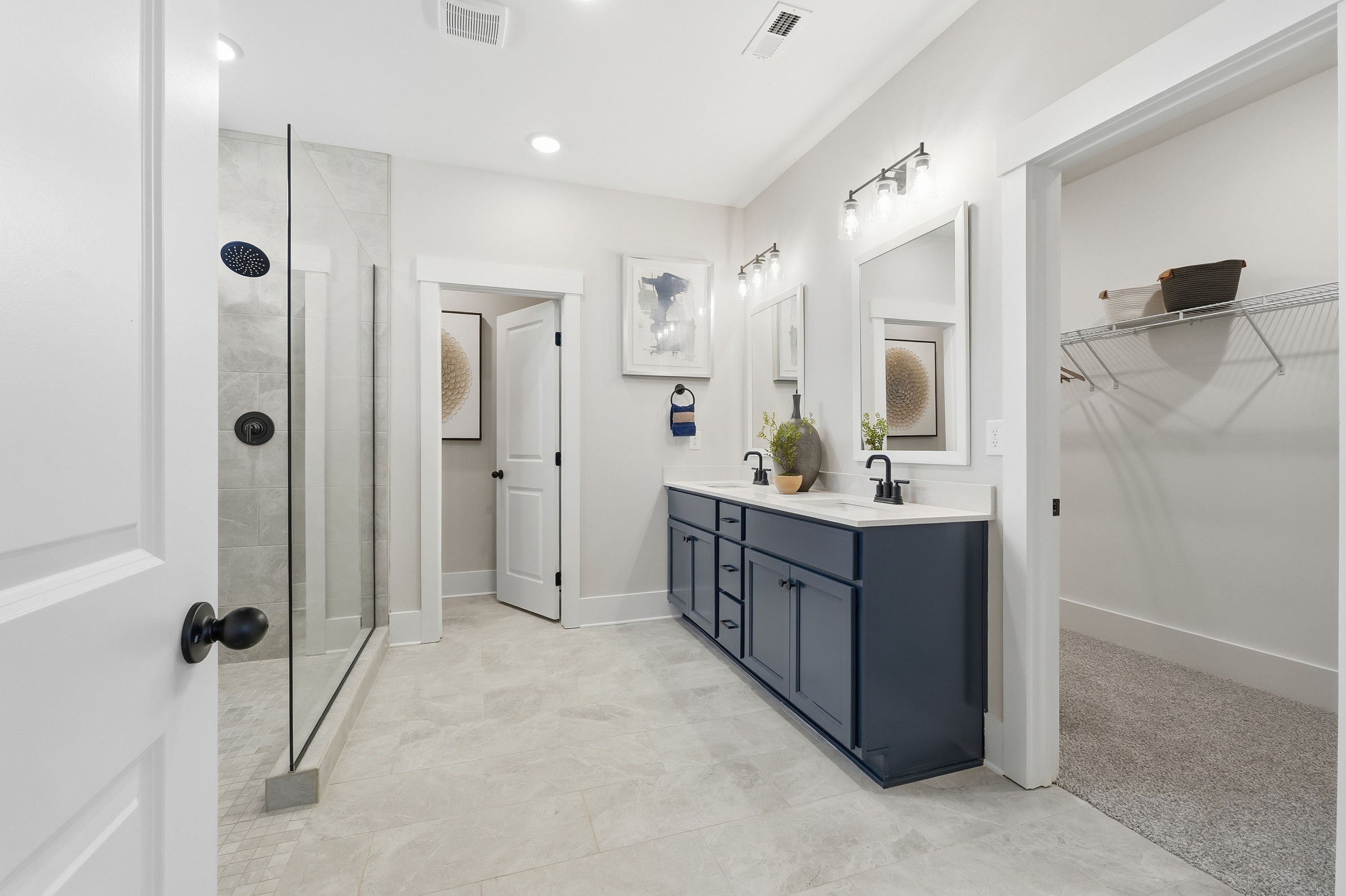 Spacious primary bathroom at Noble Ridge in Cullman Alabama with dual navy vanity, frameless glass shower, and walk-in closet