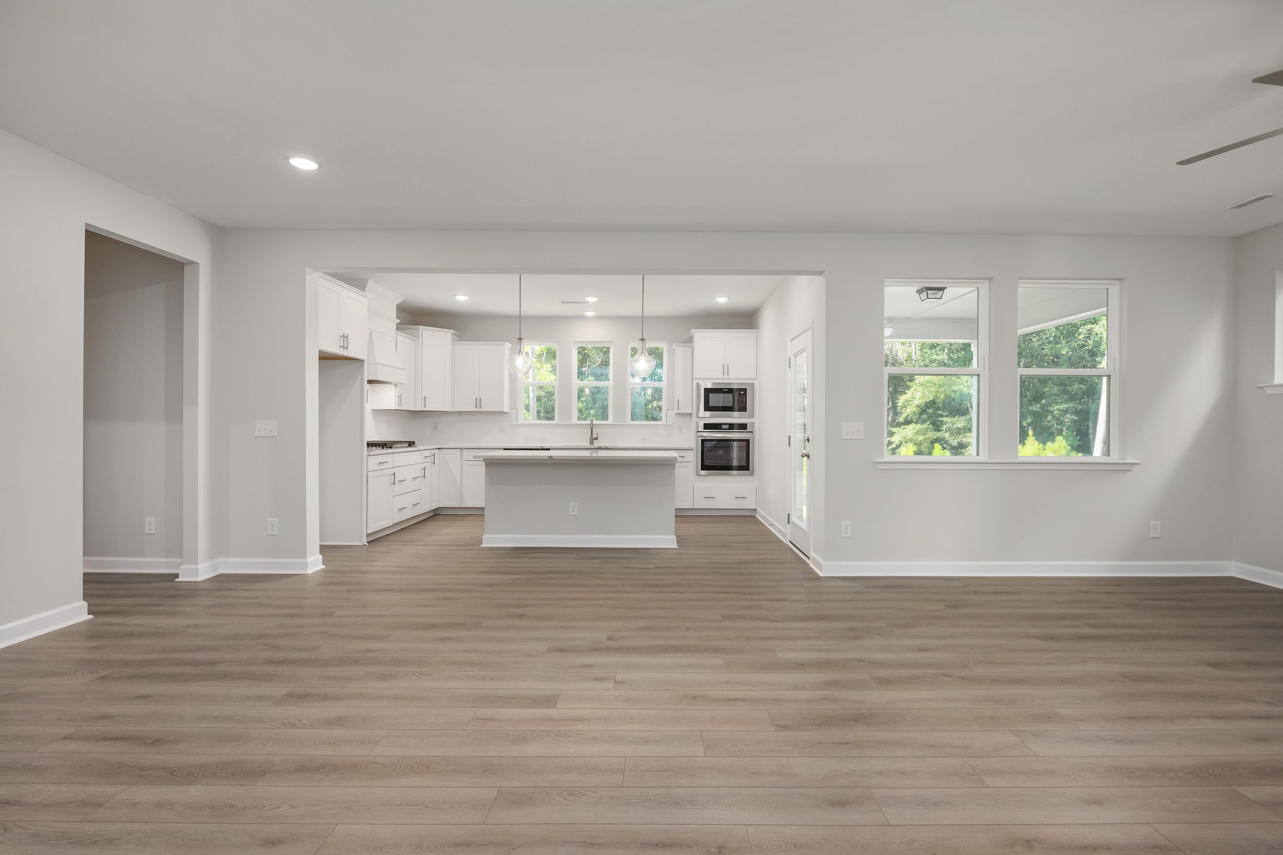 Spacious open-concept kitchen in The Aspen C with white shaker cabinets, large center island, stainless appliances, and hardwood floors