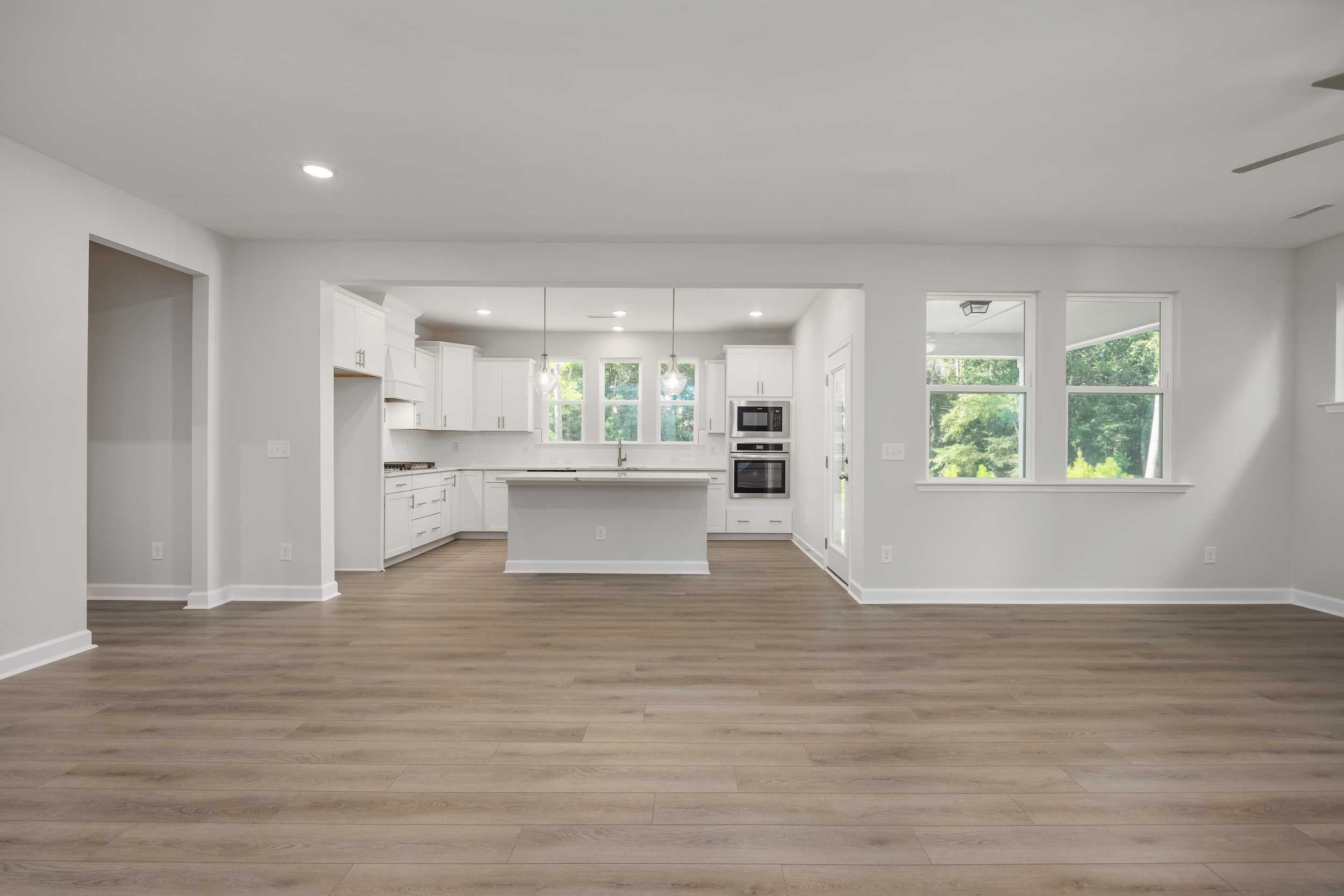 Spacious open-concept kitchen in The Aspen C with white shaker cabinets, large center island, stainless appliances, and hardwood floors