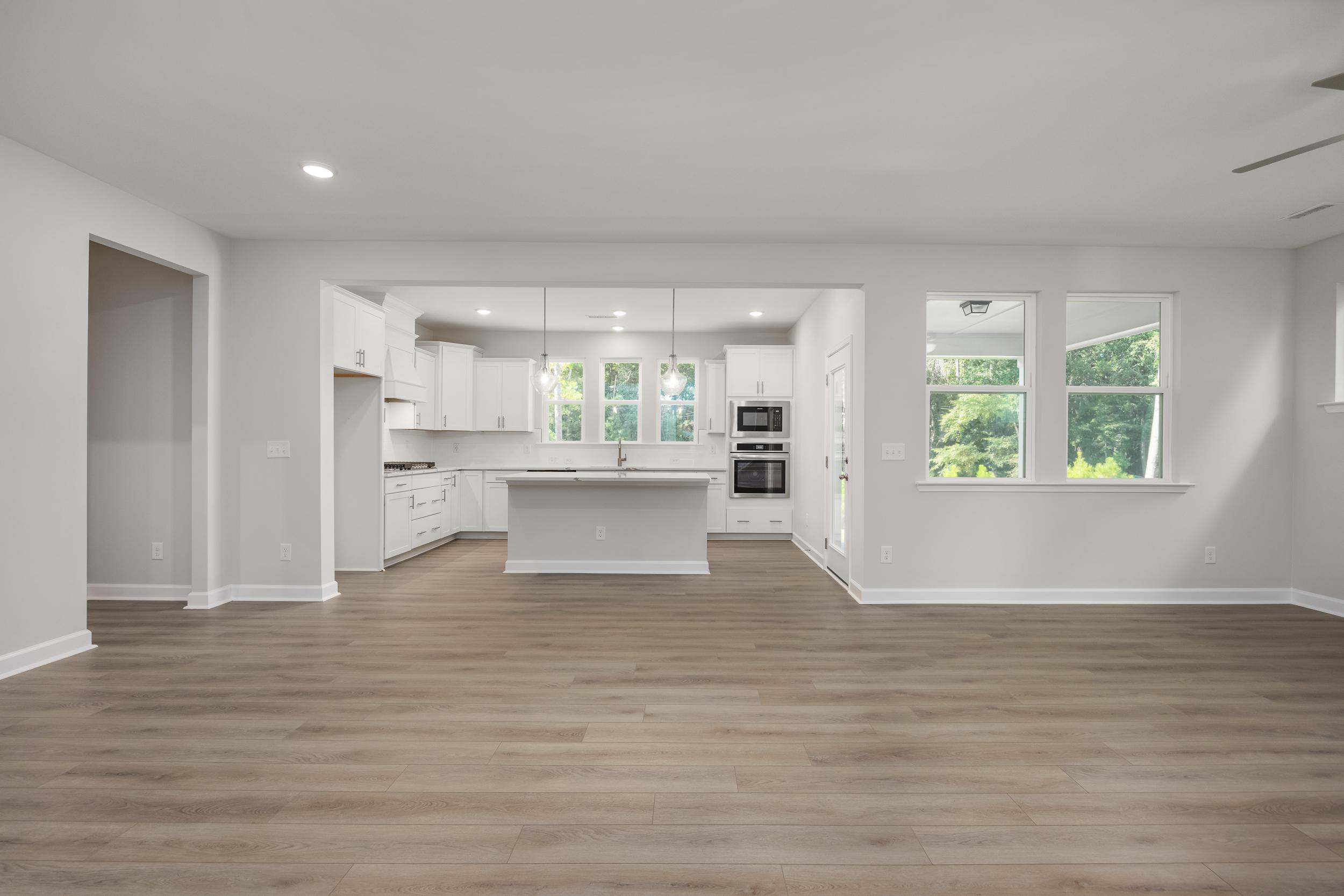 Spacious open-concept kitchen in The Aspen C with white shaker cabinets, large center island, stainless appliances, and hardwood floors