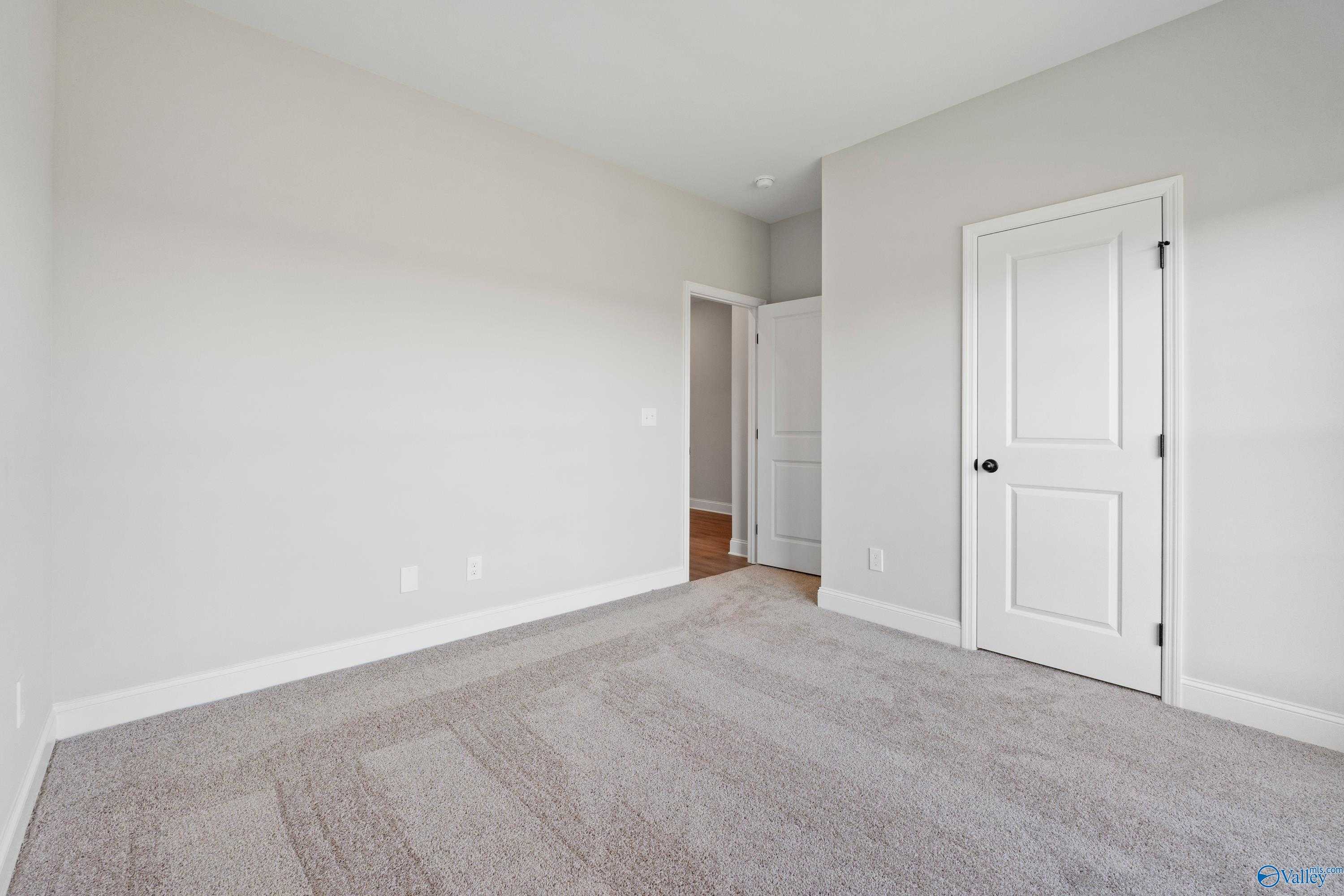 Spacious empty bedroom with light gray walls, neutral carpet, and white doors in Davidson Homes The Franklin C, Hazel Green, AL
