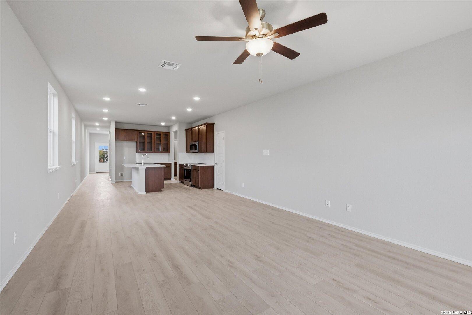 Open hallway with light laminate floors, recessed lighting, and ceiling fan leading to modern kitchen island and wood cabinets in The Frio B, San Antonio