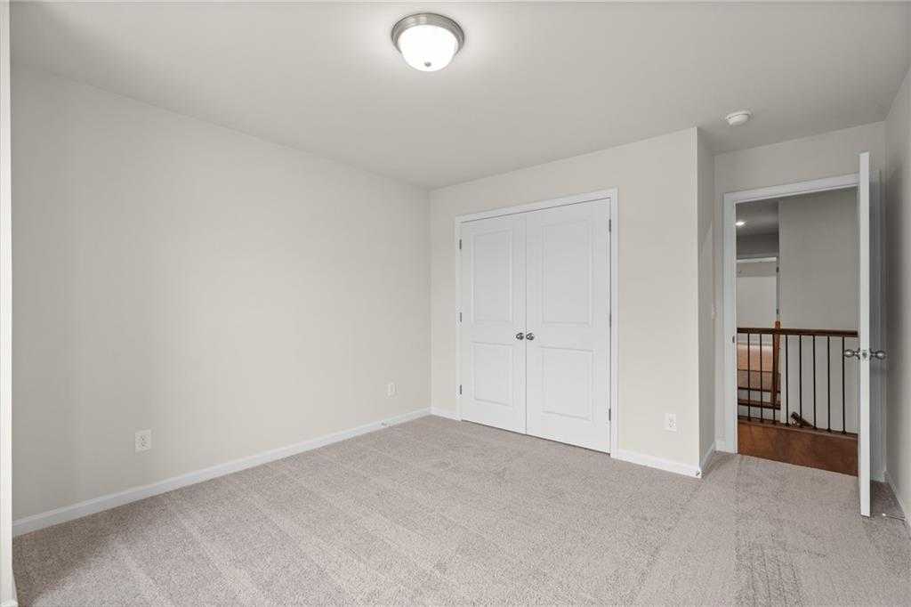 Carpeted secondary bedroom with beige walls, double closet doors, and upstairs overlook in Davidson Homes The Marion B, Kennesaw, Georgia