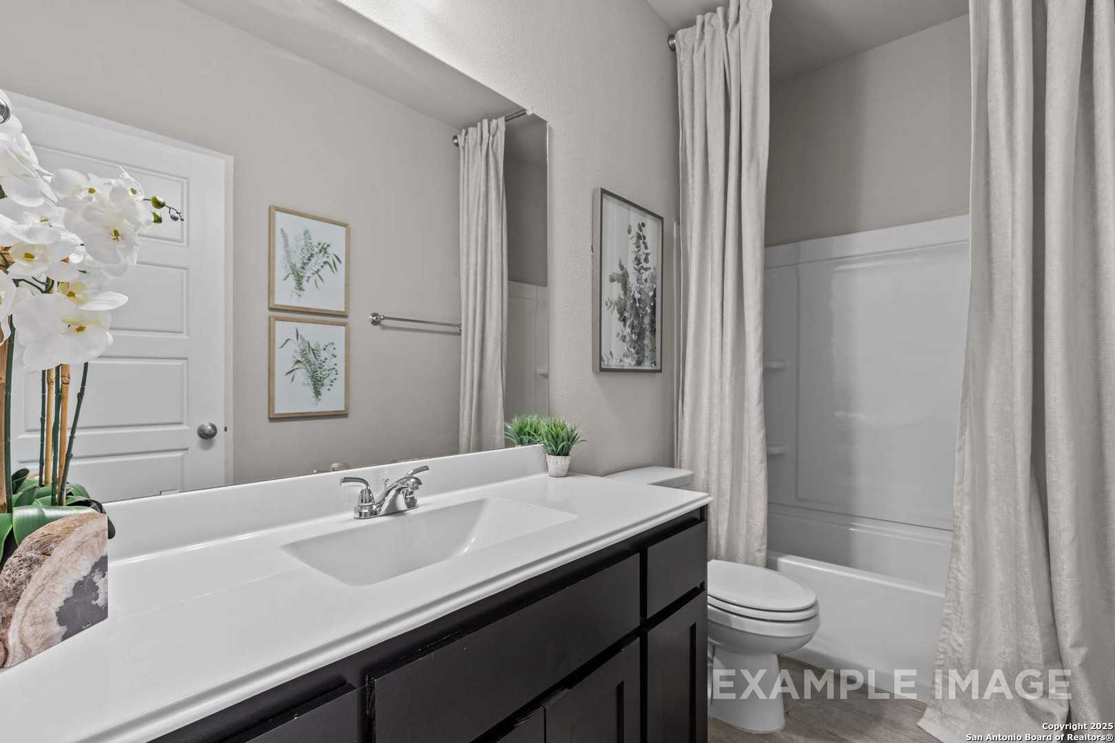 Elegant secondary bathroom with white quartz vanity, tub-shower combo, and botanical accents in Davidson Homes The Collin B, Seguin, Texas