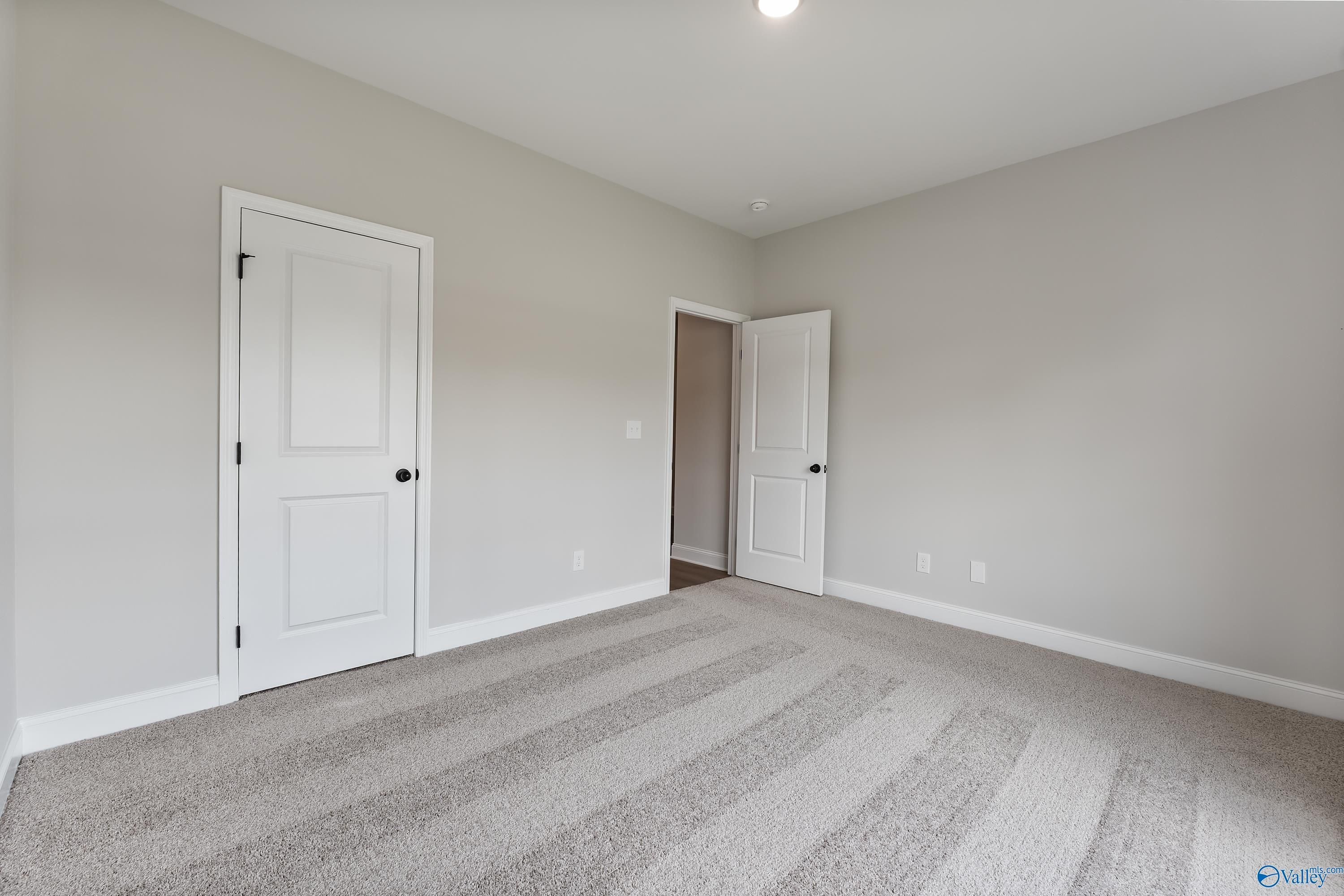 Empty secondary bedroom with light gray walls, white doors, and neutral carpet in The Daphne 4-bedroom home, Huntsville, AL